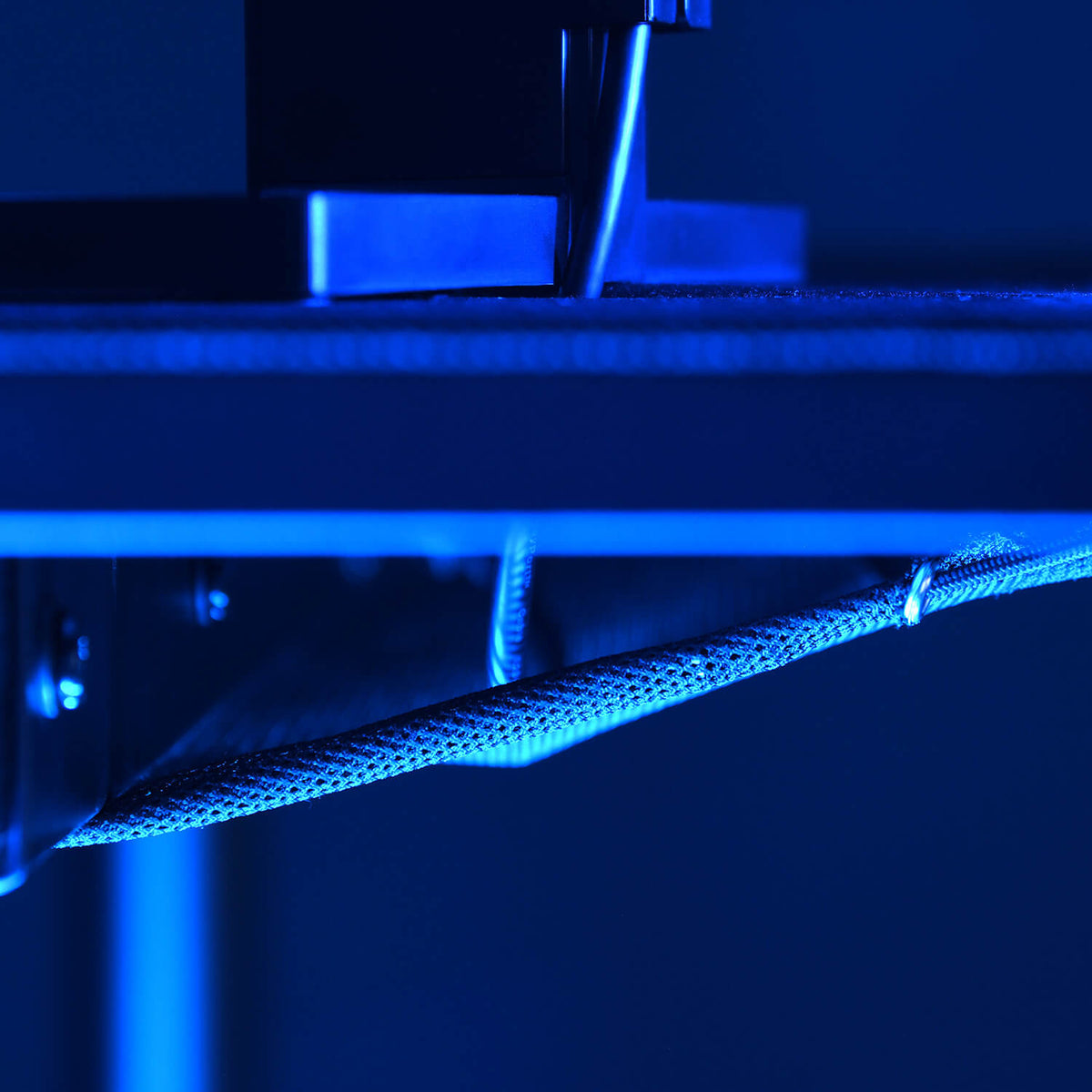 Close-up of a 3D printer nozzle printing an object under blue lighting.