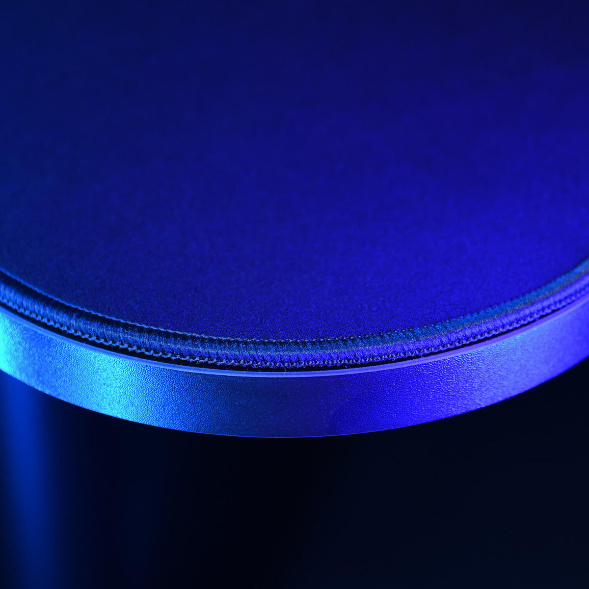 Close-up of a round, blue-lit surface with textured stitching near the edge.