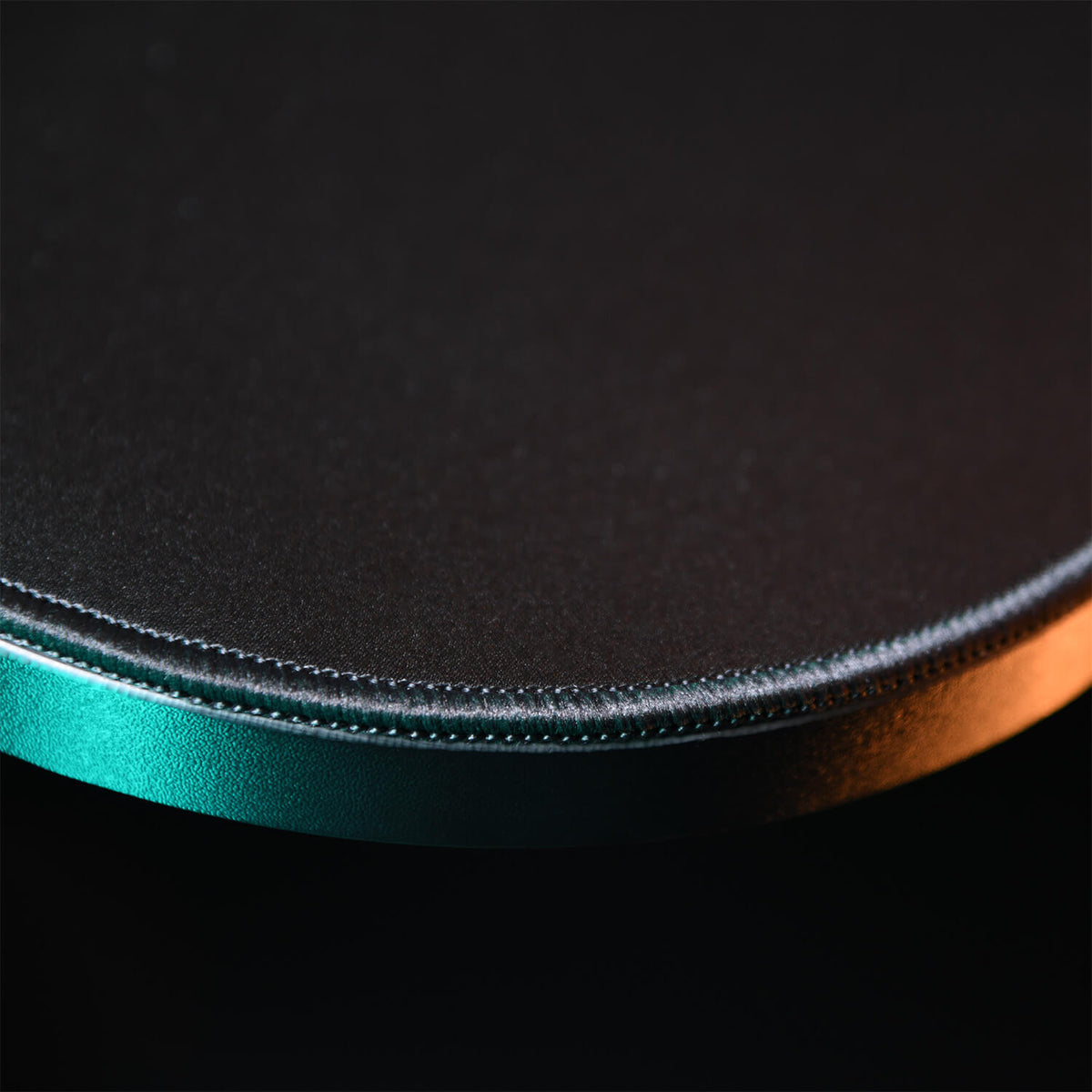 Close-up of the edge of a round, metallic object with teal and orange lighting.