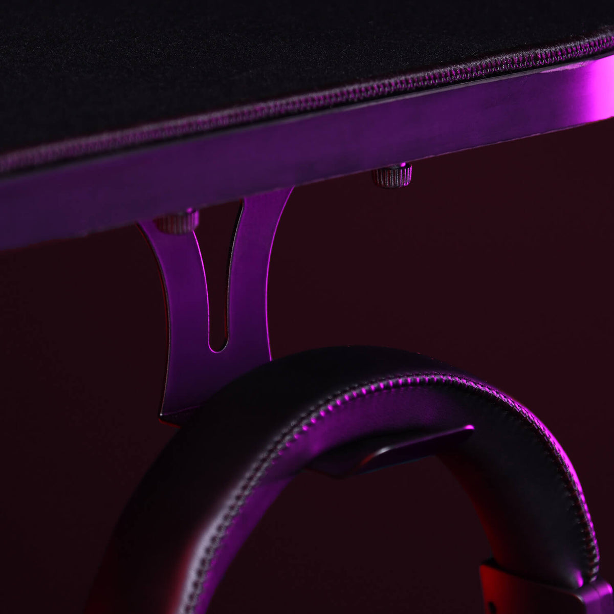 A close-up of a headphone holder attached under a desk, lit with purple lighting.