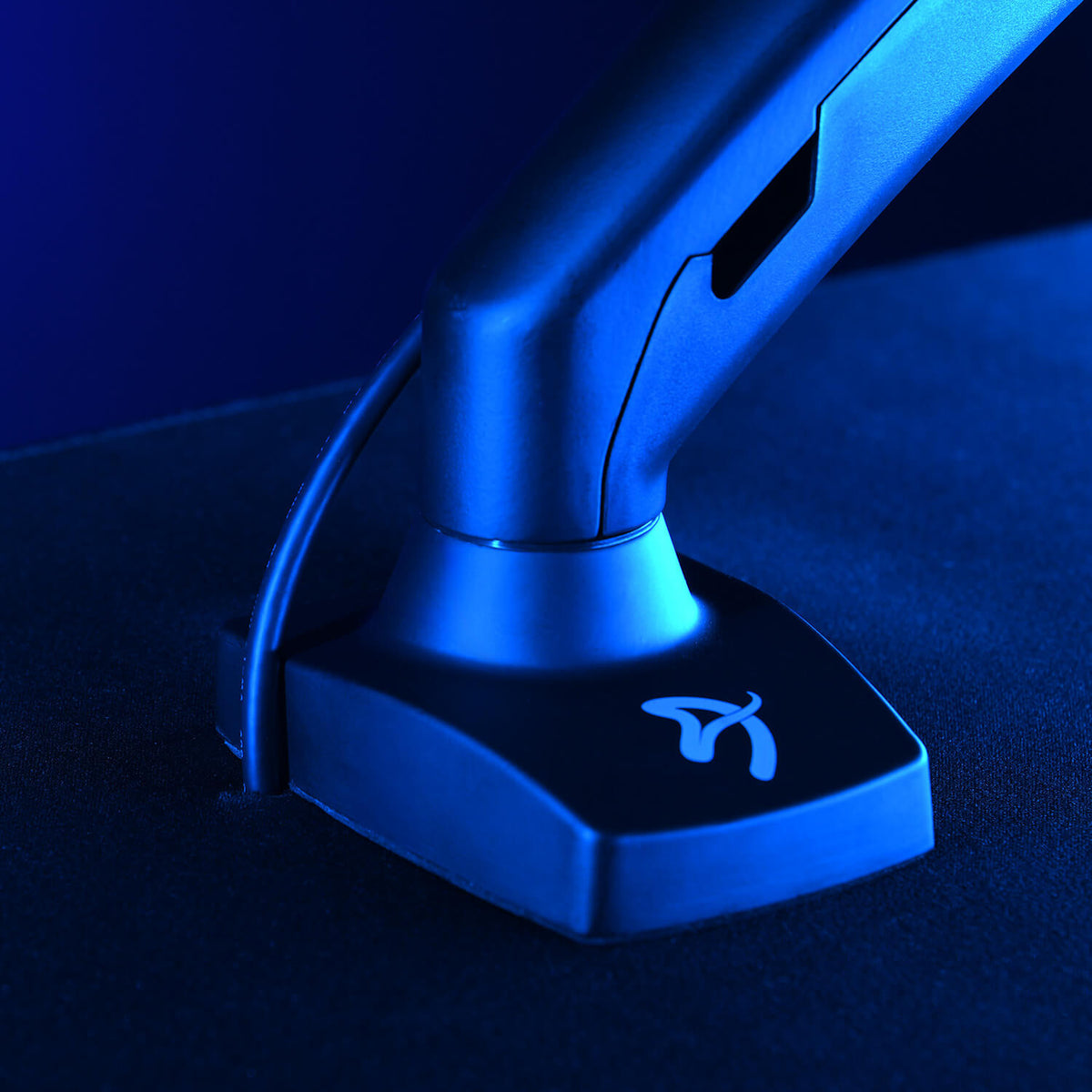 A monitor arm base with a cable, lit by blue light, on a dark surface.