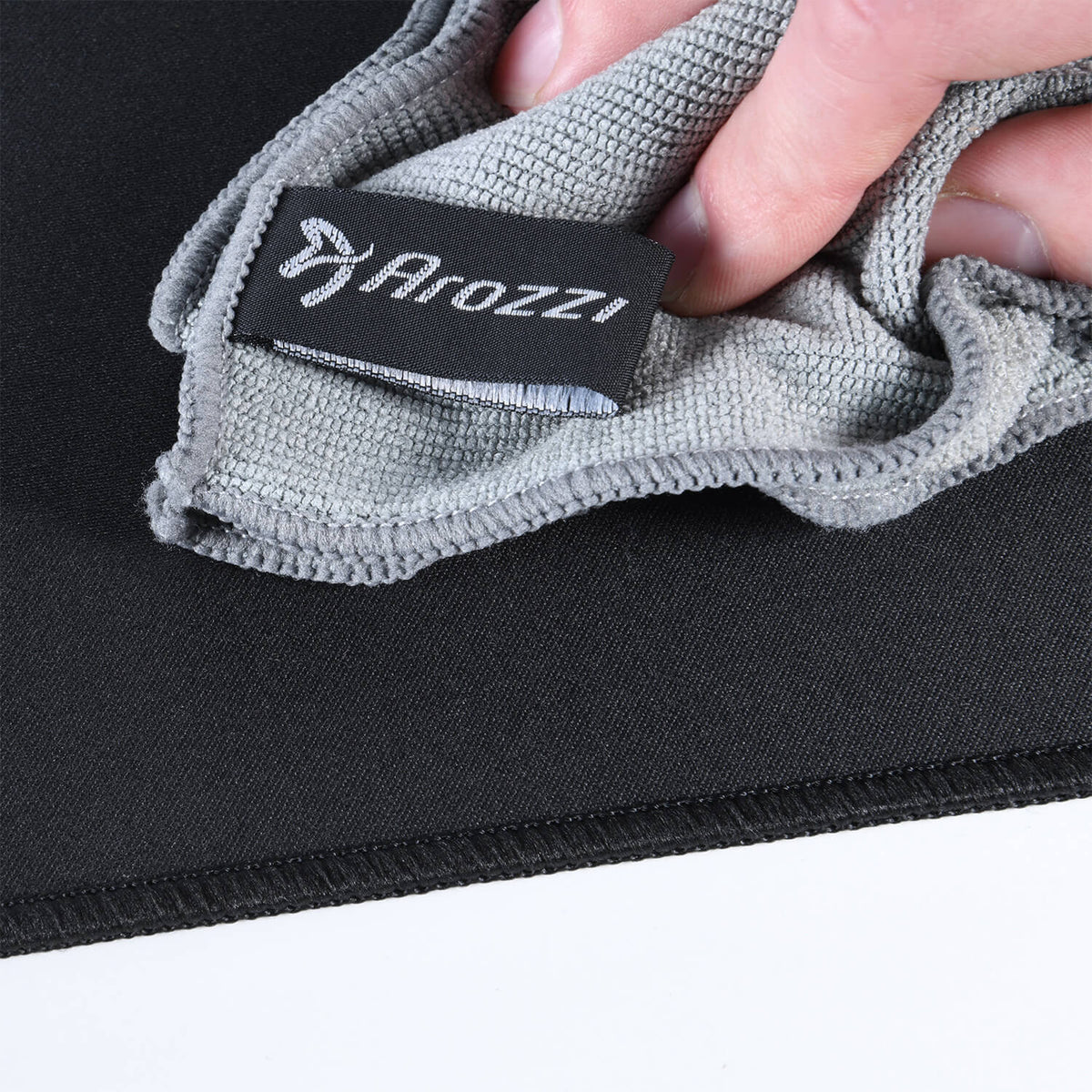 Hand cleaning a black surface with a gray cloth labeled Arozzi on a black background.