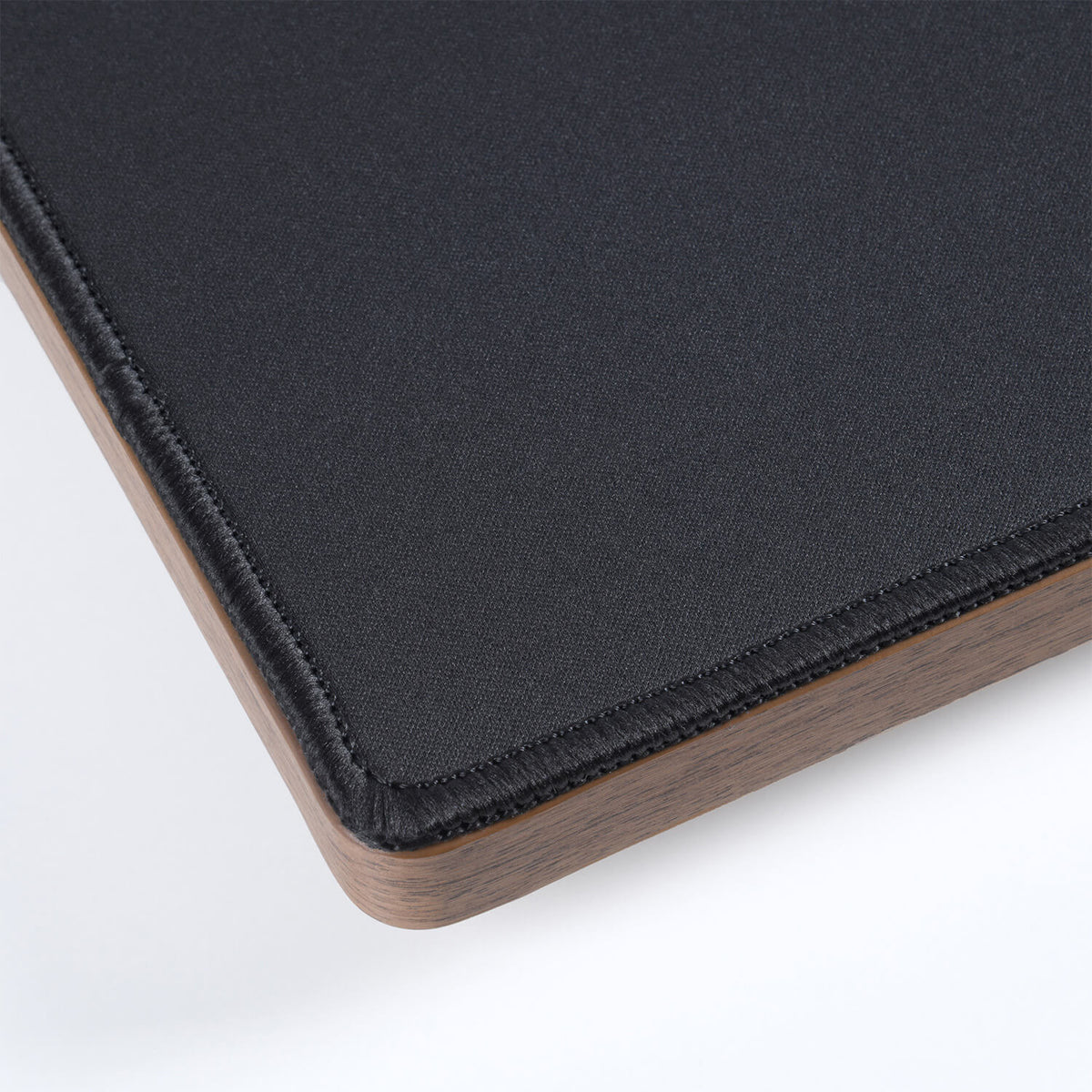 Corner of a black fabric mouse pad with a wooden base, shown on a white background.