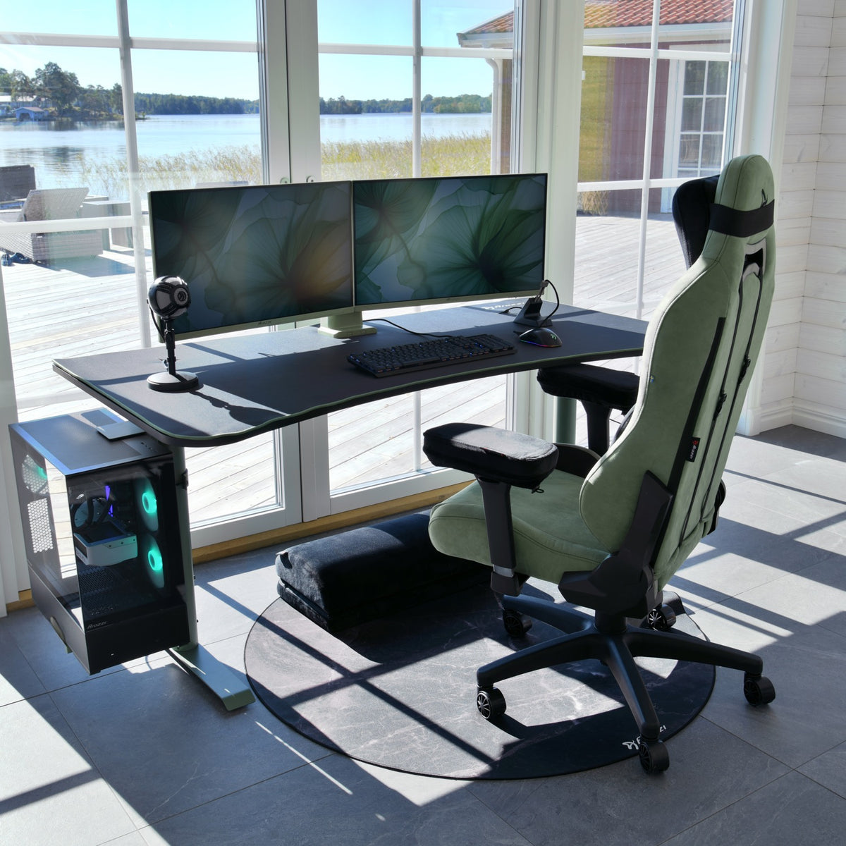 Arozzi Arena Gaming Desk setup with dual monitors, gaming chair, mouse pad, lakeside view.