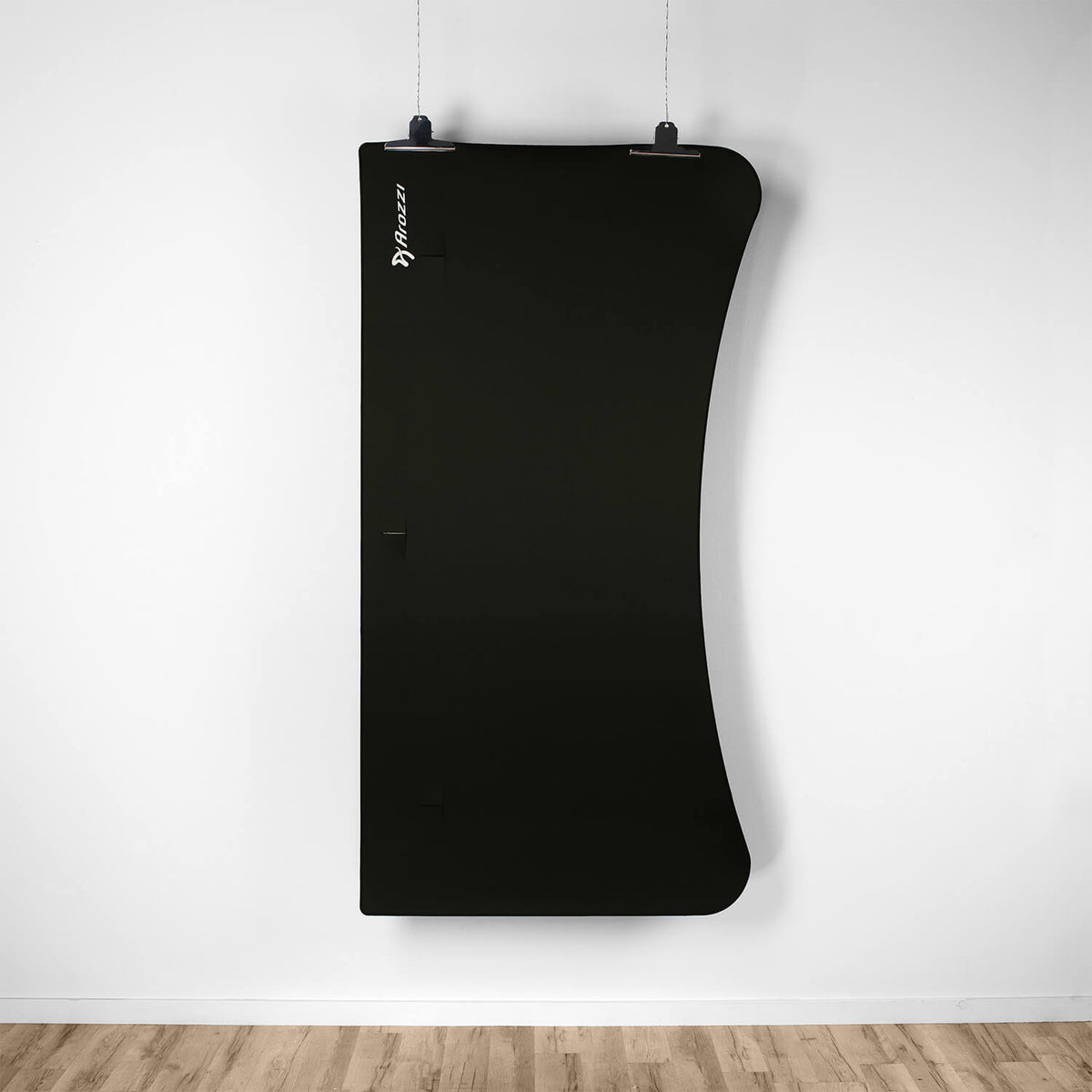 Curved black Arozzi Europe Arena Mousepad hanging on a white wall above a light wood floor.