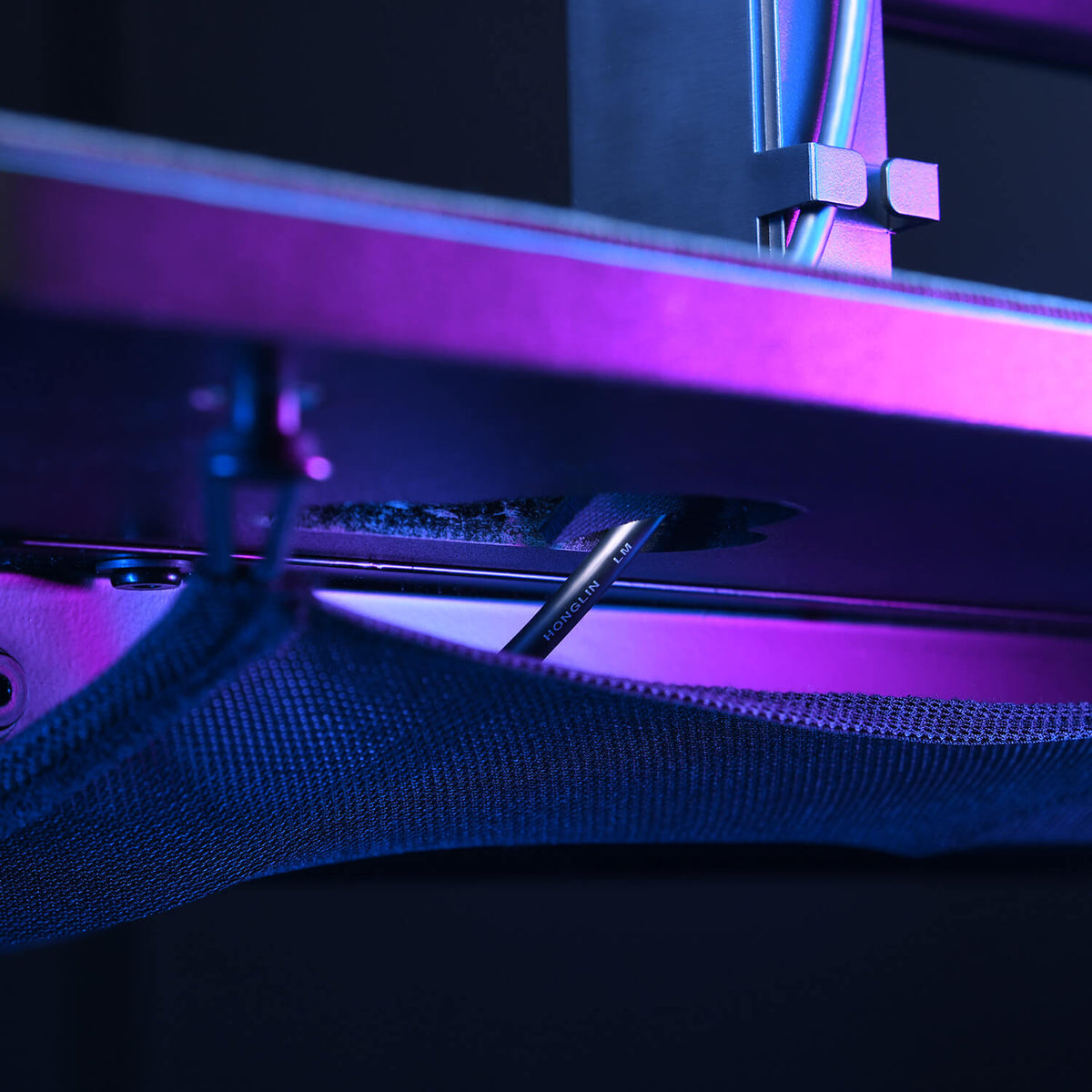 A close-up of cables and fabric under a desk, lit by purple and blue light.
