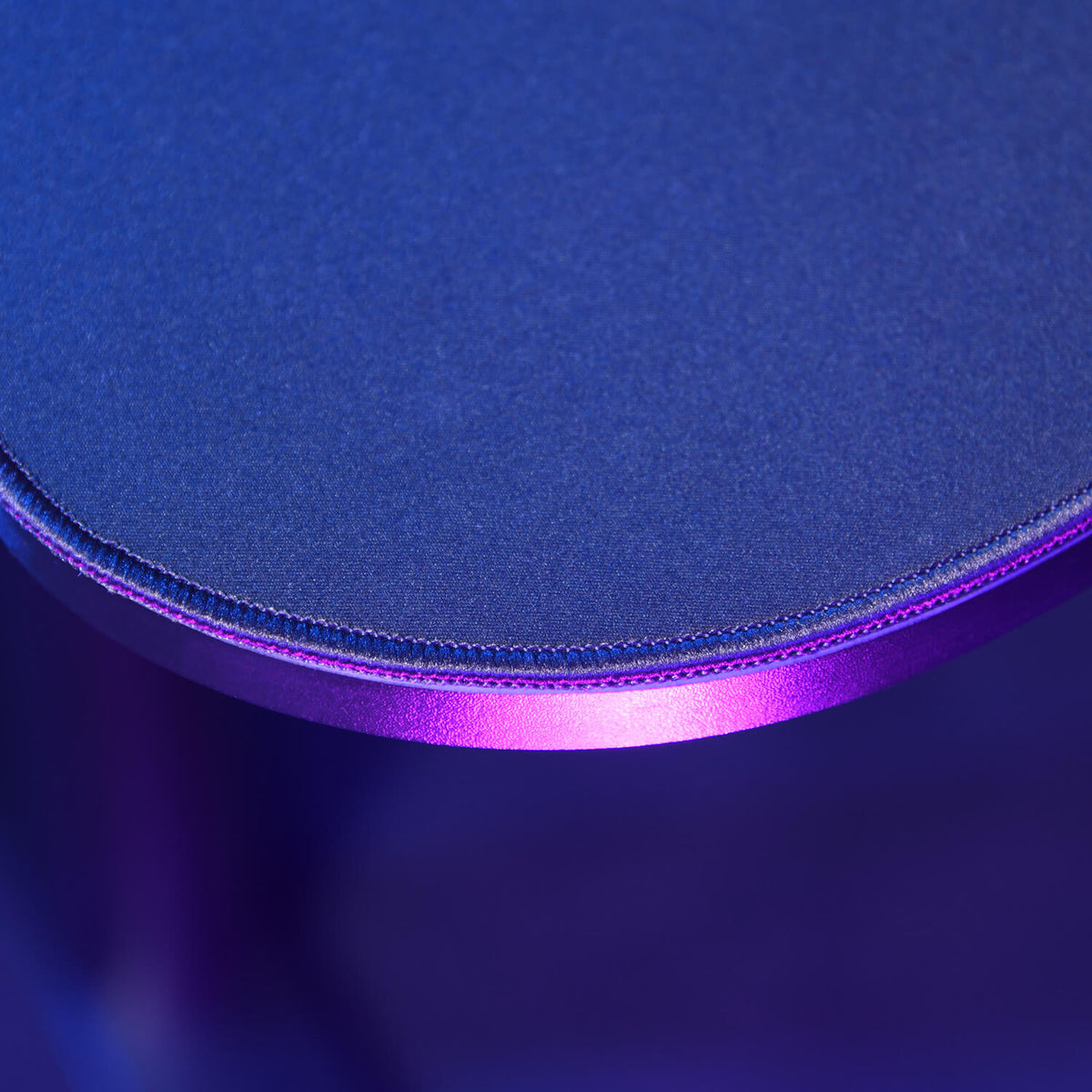 Close-up of a round blue tabletop with purple lighting and visible stitching on the edge.