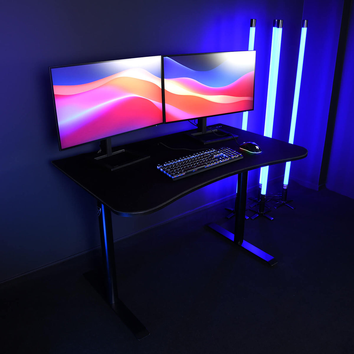 Dual monitors, keyboard, and mouse on an Arozzi Arena Gaming Desk - Small with blue LED lights.