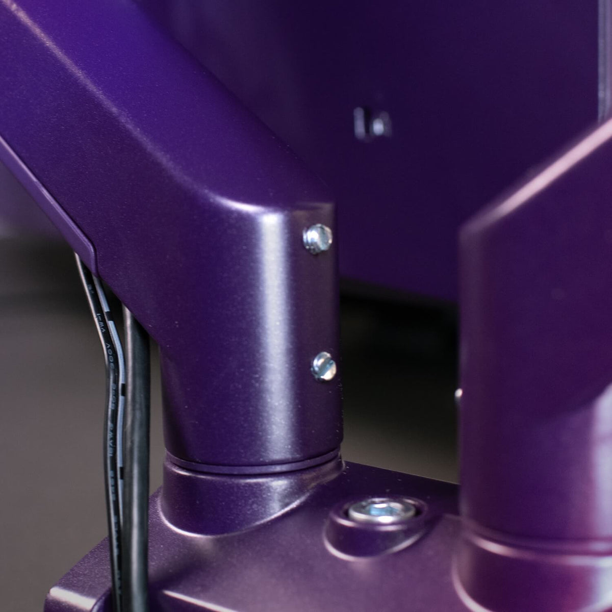 Close-up of a metallic purple machine arm with visible bolts and black cables attached.
