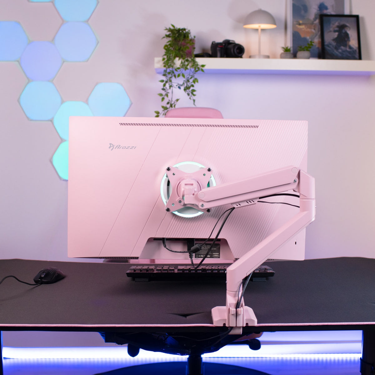 A pink Arozzi Alzare Neo Single gas spring arm holds a monitor in a modern, minimalist workspace.