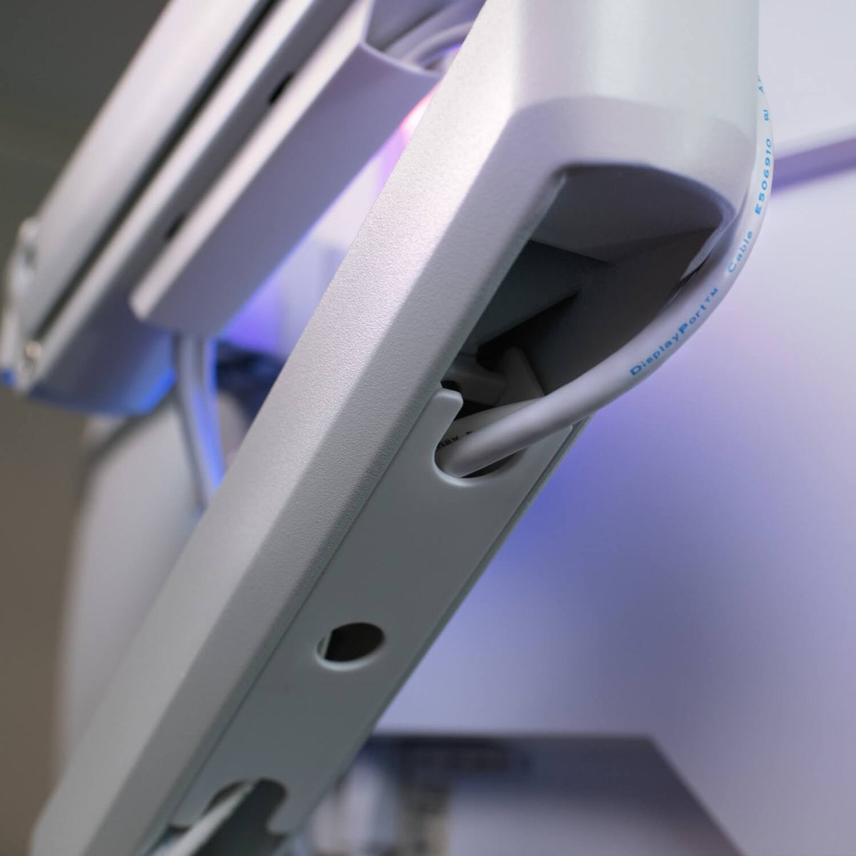 Close-up of a white cable guided through a slot in a gray plastic arm with soft lighting.