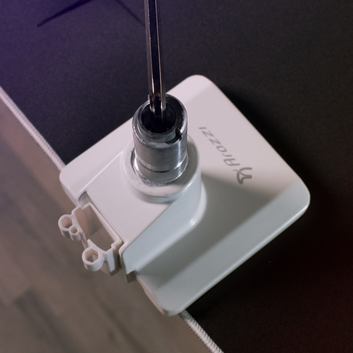 A screwdriver is inserted into a metal cylinder on a white Arozzi chair part by a desk edge.