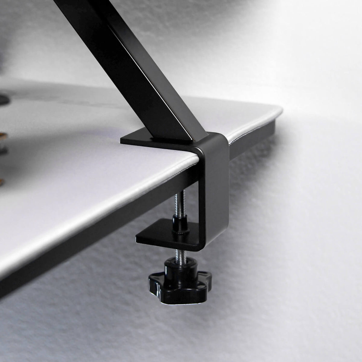 Arozzi Europe Desk Riser - Small clamps in black metal to a white desk’s edge.