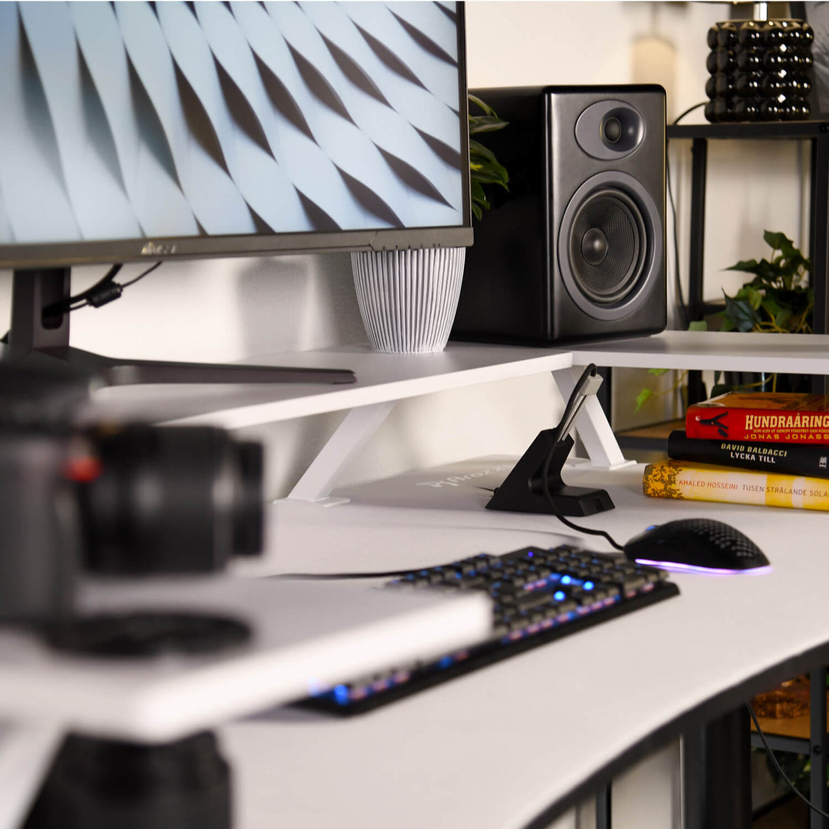 Curved monitor on Arozzi Europe Desk Riser - Small, with keyboard, speaker, books, and plants.