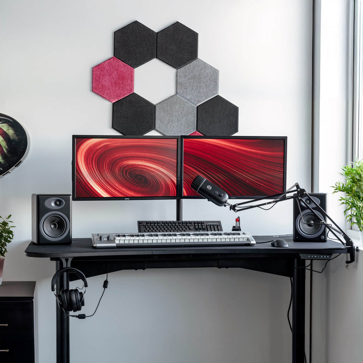 Dual monitors on black desk with keyboard, speakers, plants, and Arozzi Europe Headset Hanger.