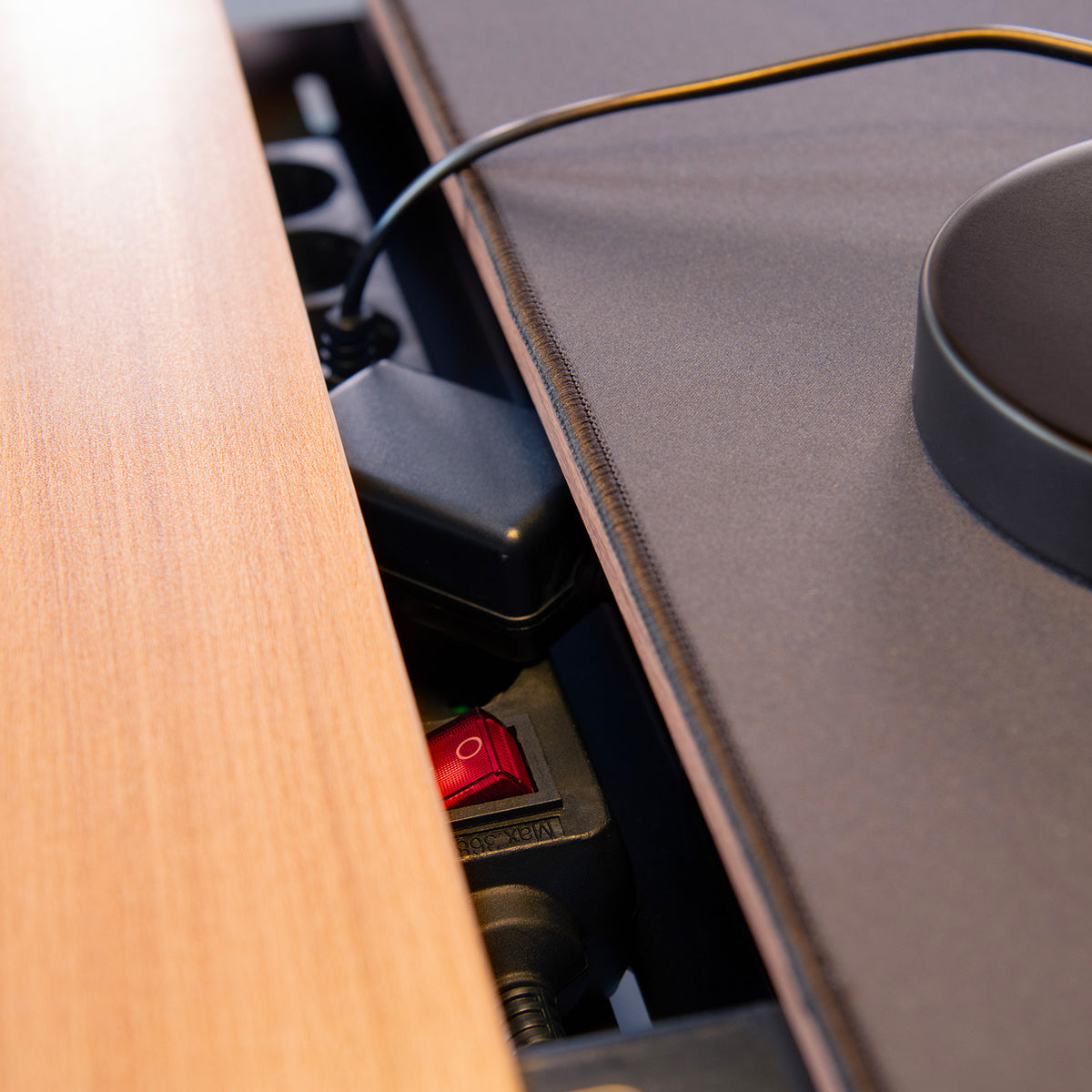 Power strip with red switch and cable between a wooden desk and a black surface.