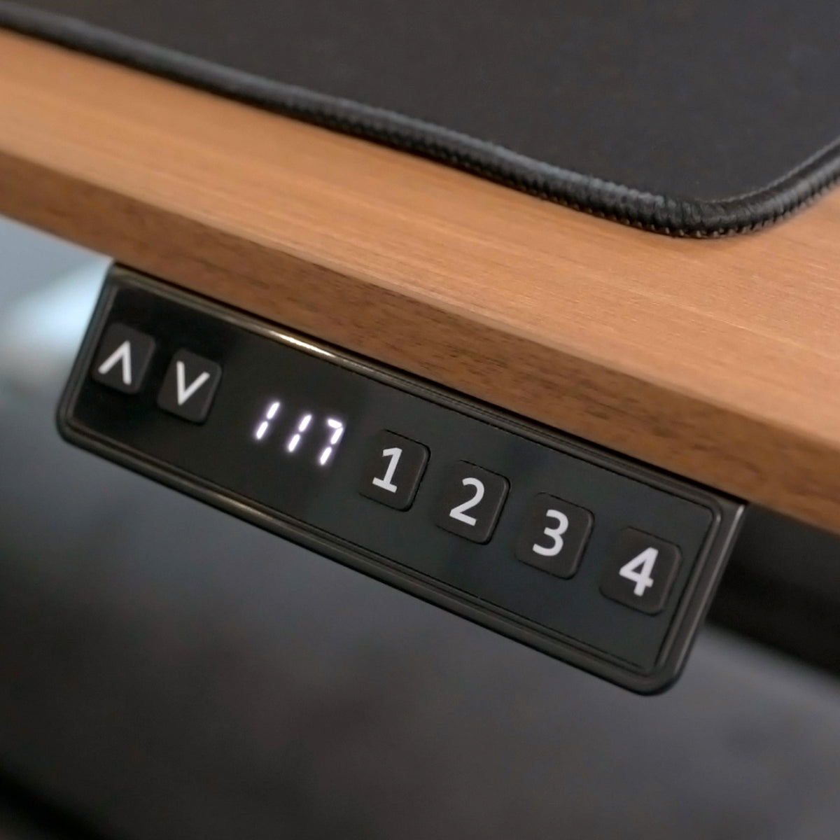 Close-up of an electric desk control panel with arrow and number buttons displaying 117.