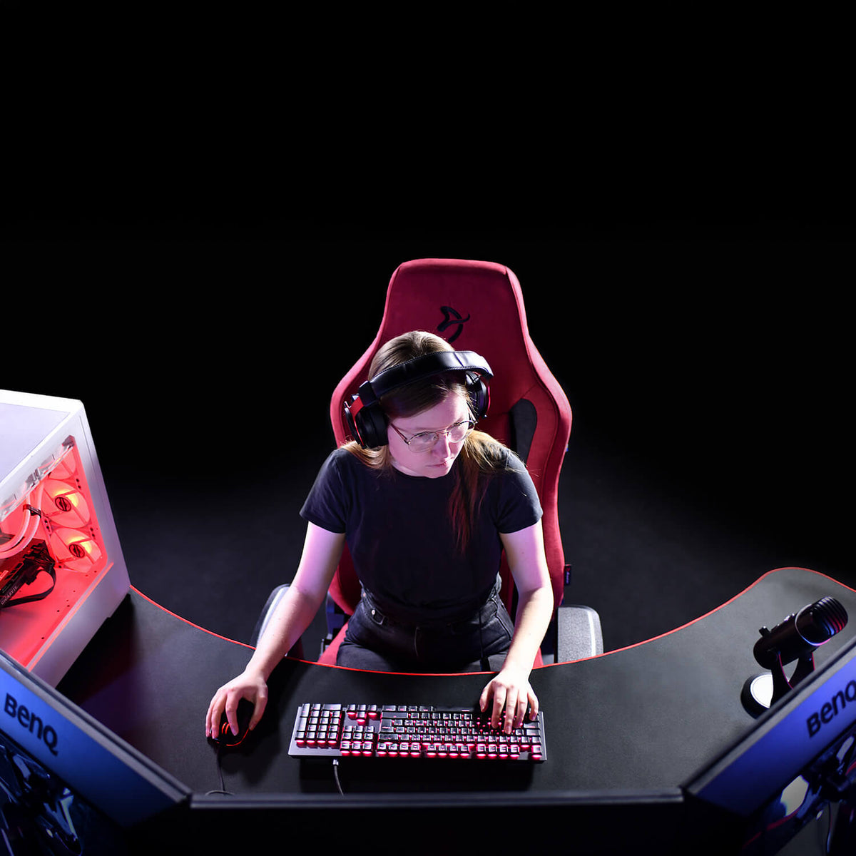 A person with headphones gaming on a PC at a curved desk with two monitors.