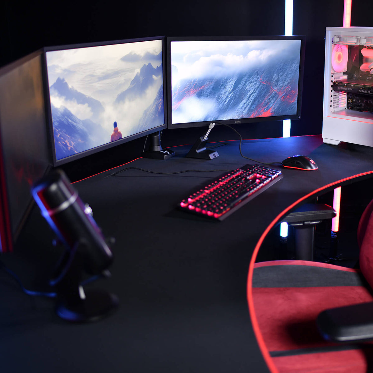 Dual monitors, gaming keyboard, mouse, mic, and PC tower on a curved black desk.