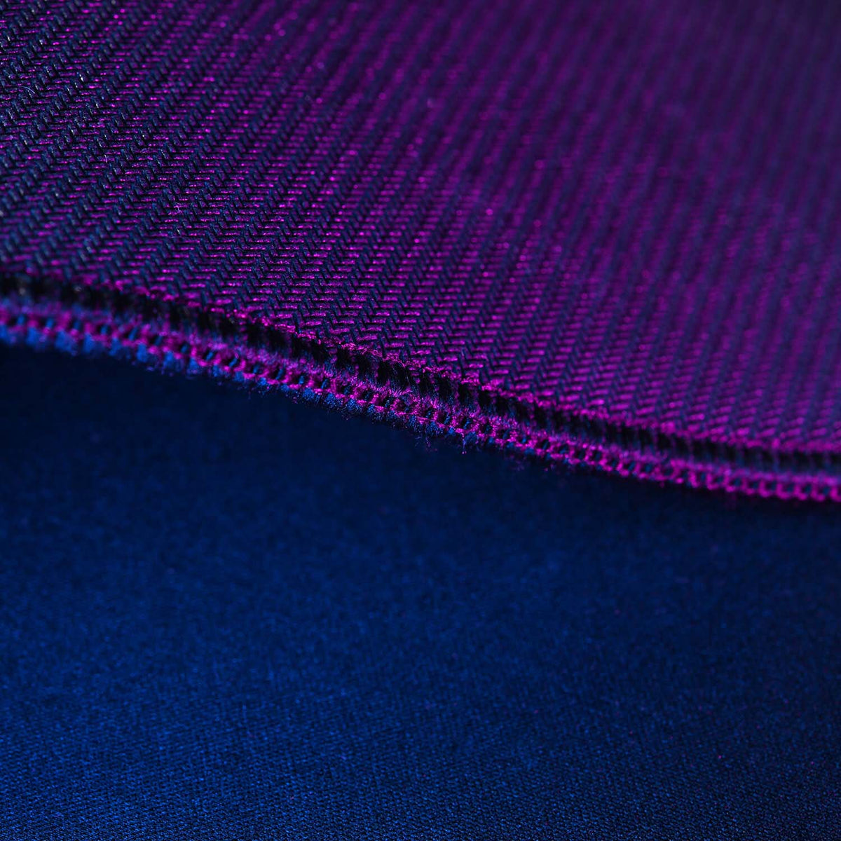 Close-up of purple woven fabric edge on top of smooth dark blue fabric.