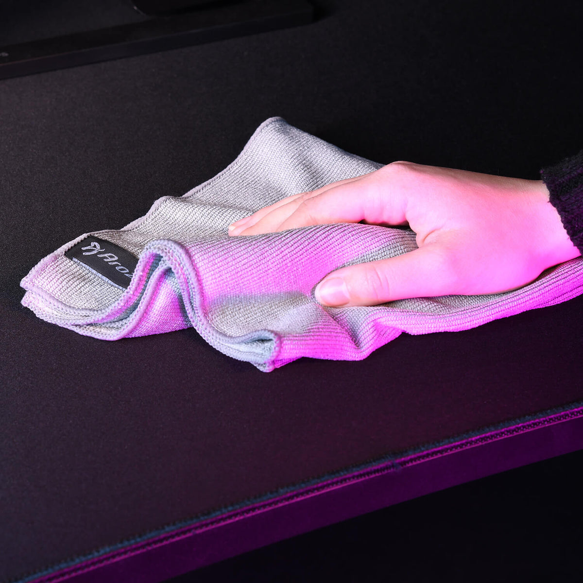 Hand wiping a black surface with a gray cloth under pink lighting.