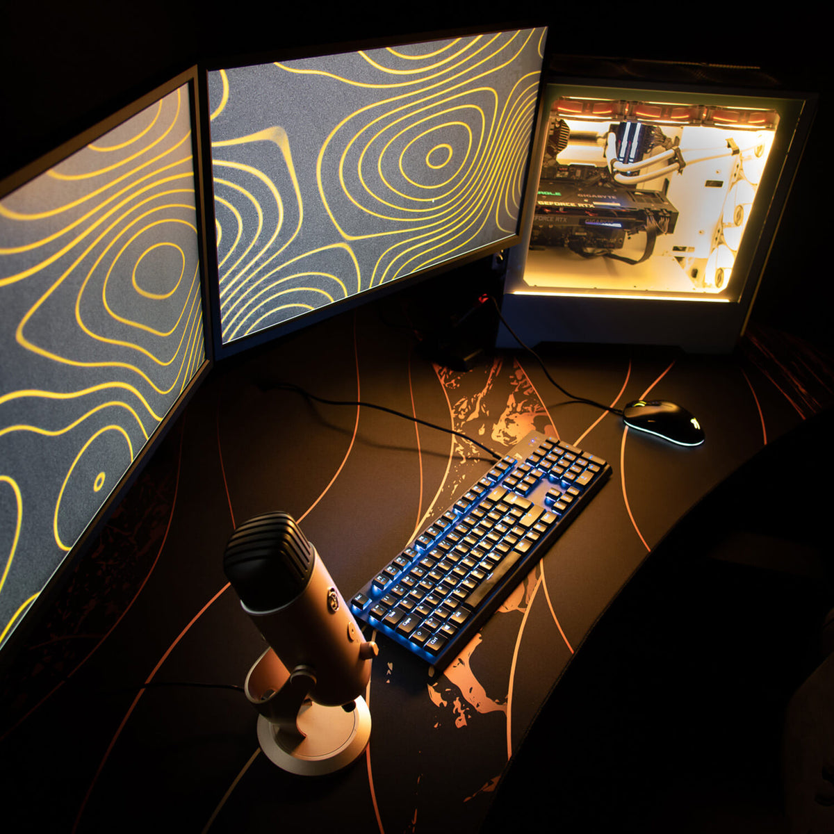 Dual monitors, lit keyboard, and PC tower rest on an Arozzi Europe Arena Mousepad atop desk.