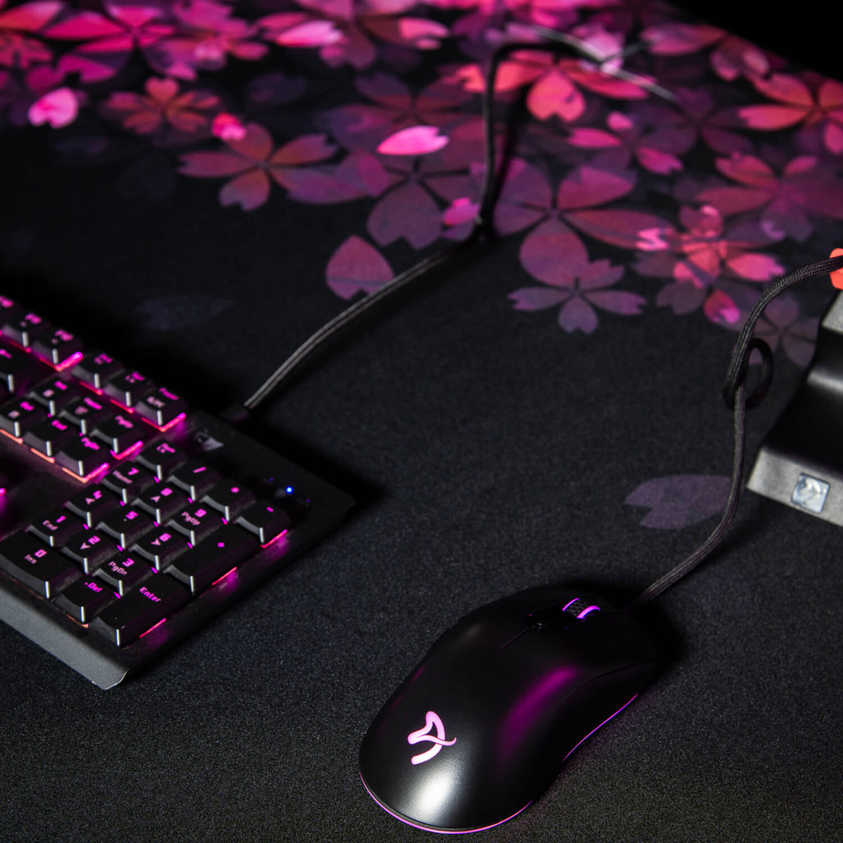 A black gaming mouse and keyboard on an Arozzi Europe Arena Mousepad with pink floral design.