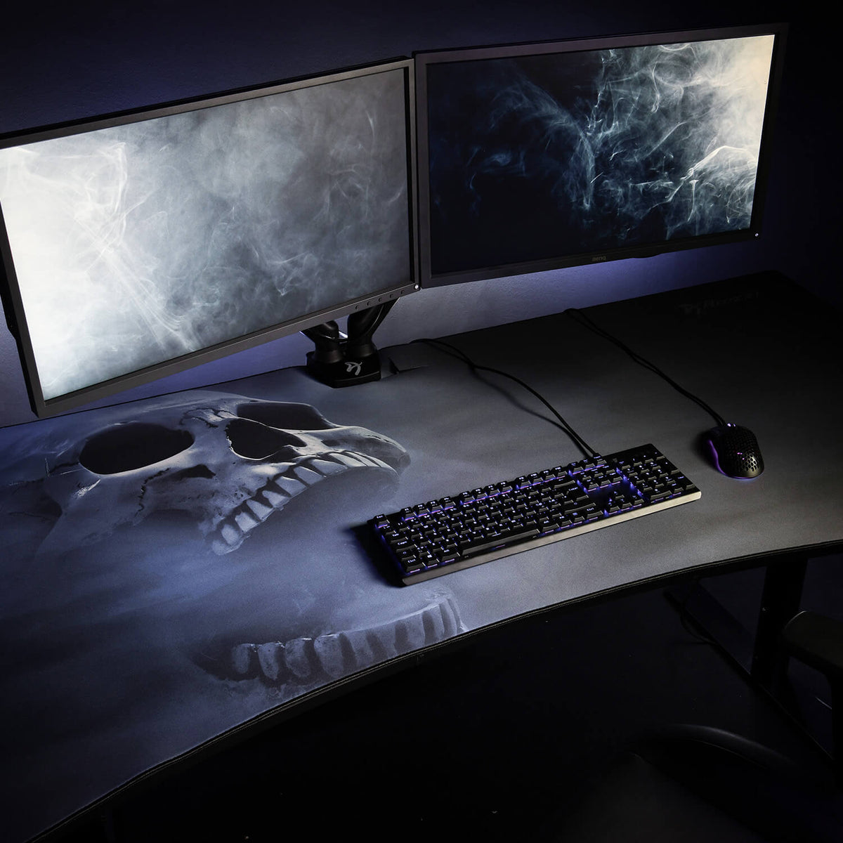 Dual monitors on a desk with an Arozzi Europe Arena Mousepad, keyboard, mouse, and skull design.