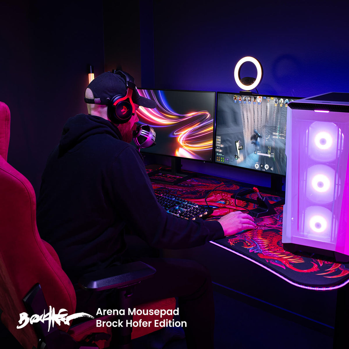 Gamer at dual monitors on Arozzi Arena Gaming Desk, large mouse pad, headset in dark room.