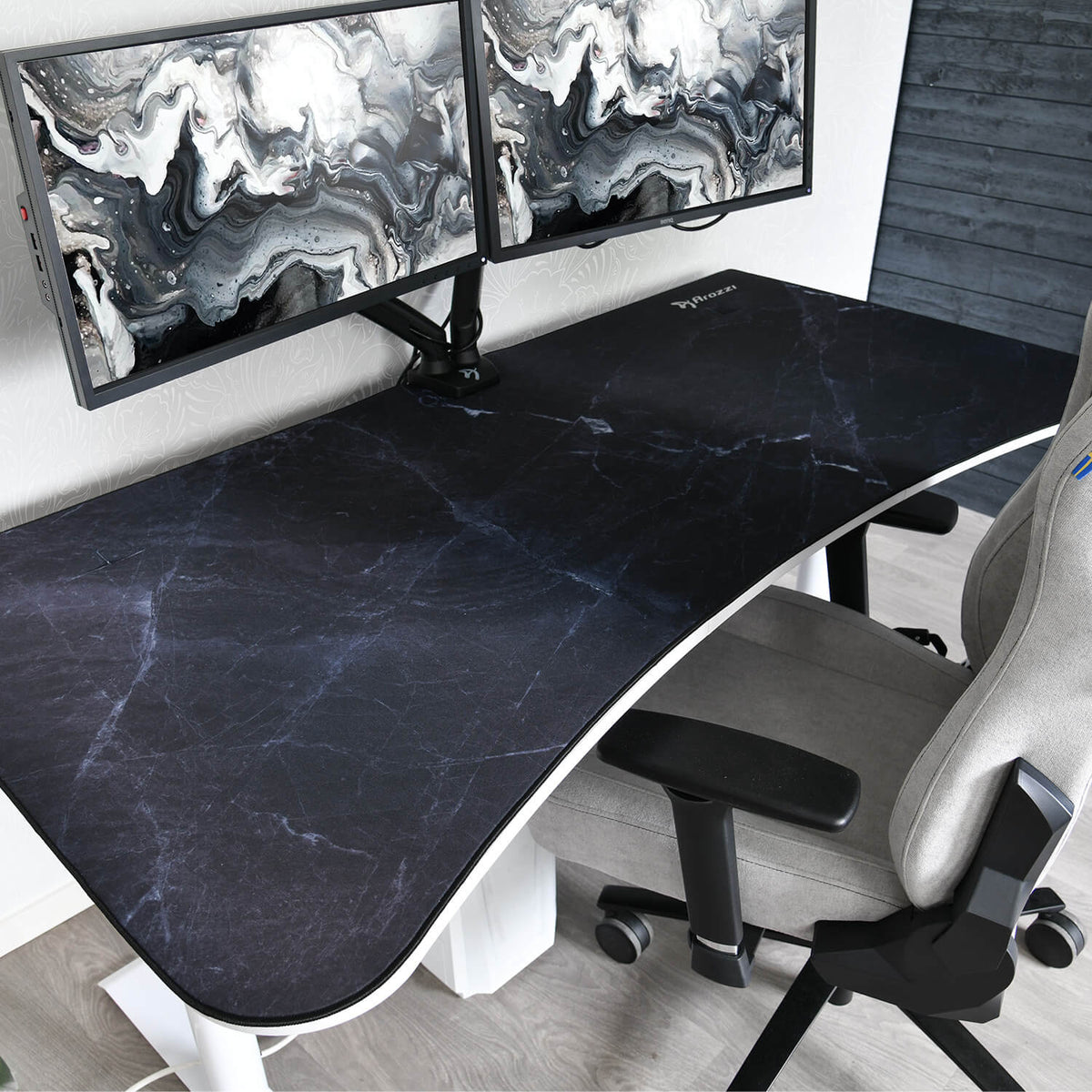 Dual monitors on a black Arena Mousepad by Arozzi Europe, beside a gray chair in a modern workspace.