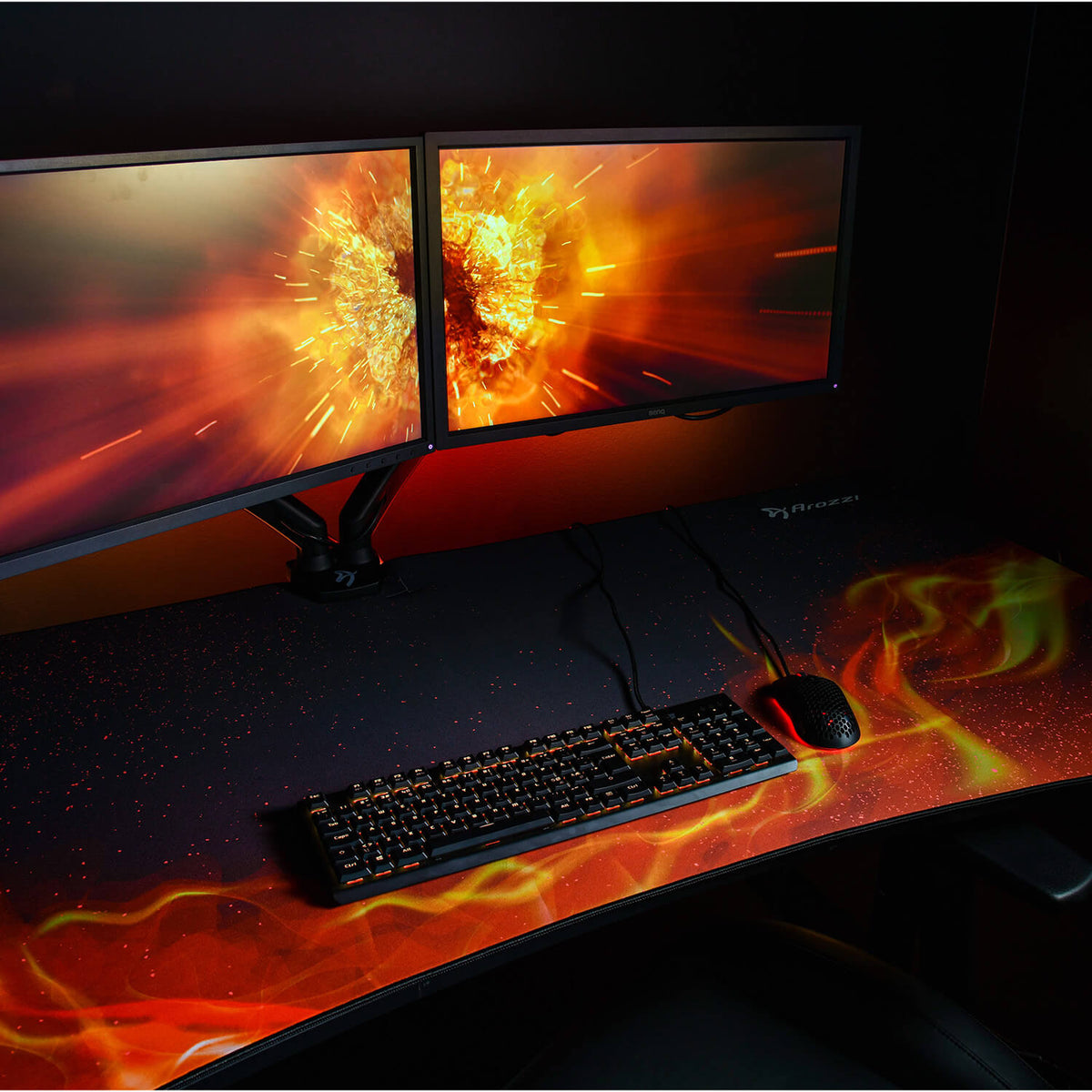 Dual monitors, keyboard, and mouse on an Arozzi Europe Arena Mousepad with explosion wallpaper.