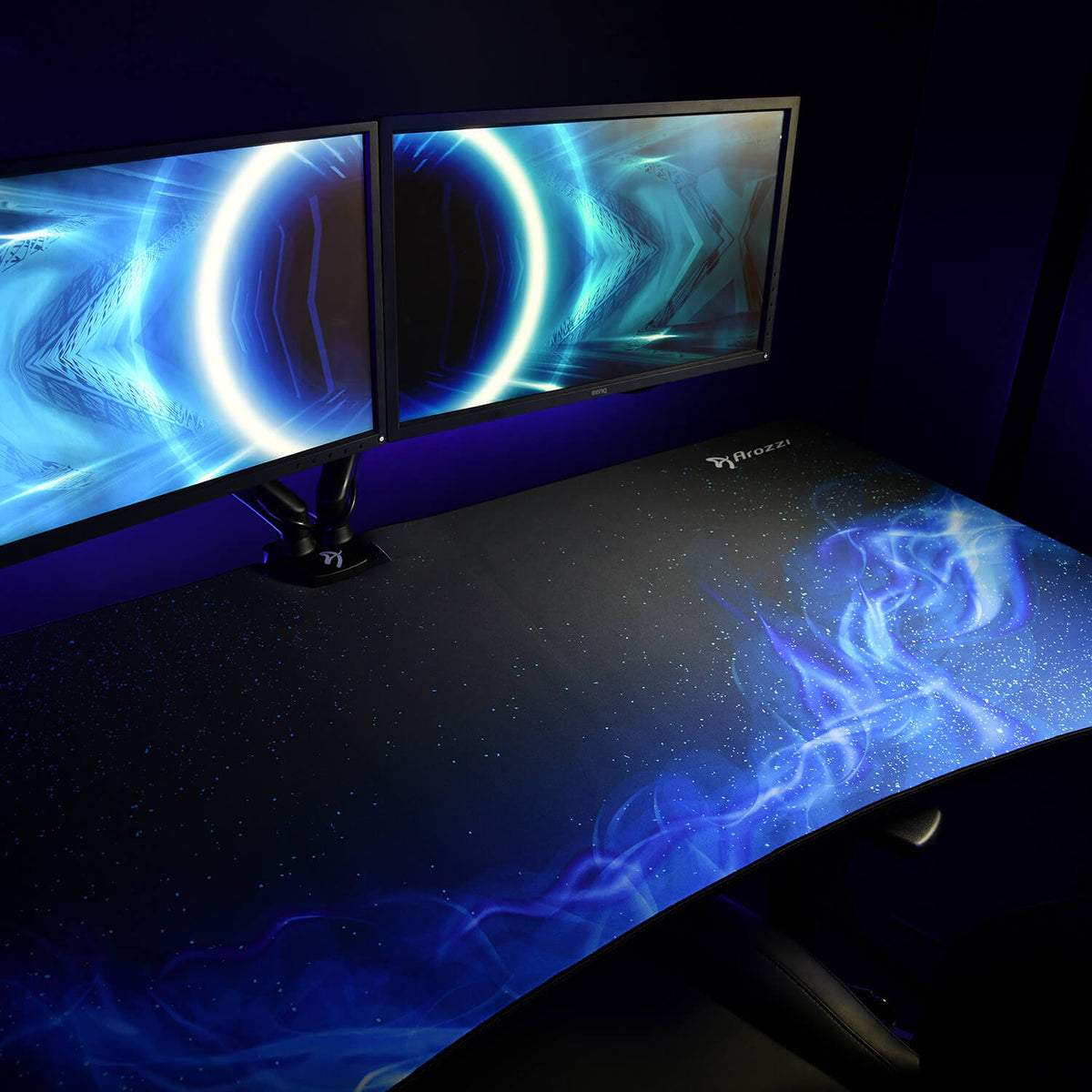 Dual monitors on an Arena Mousepad by Arozzi Europe in a dark room with blue abstract graphics.