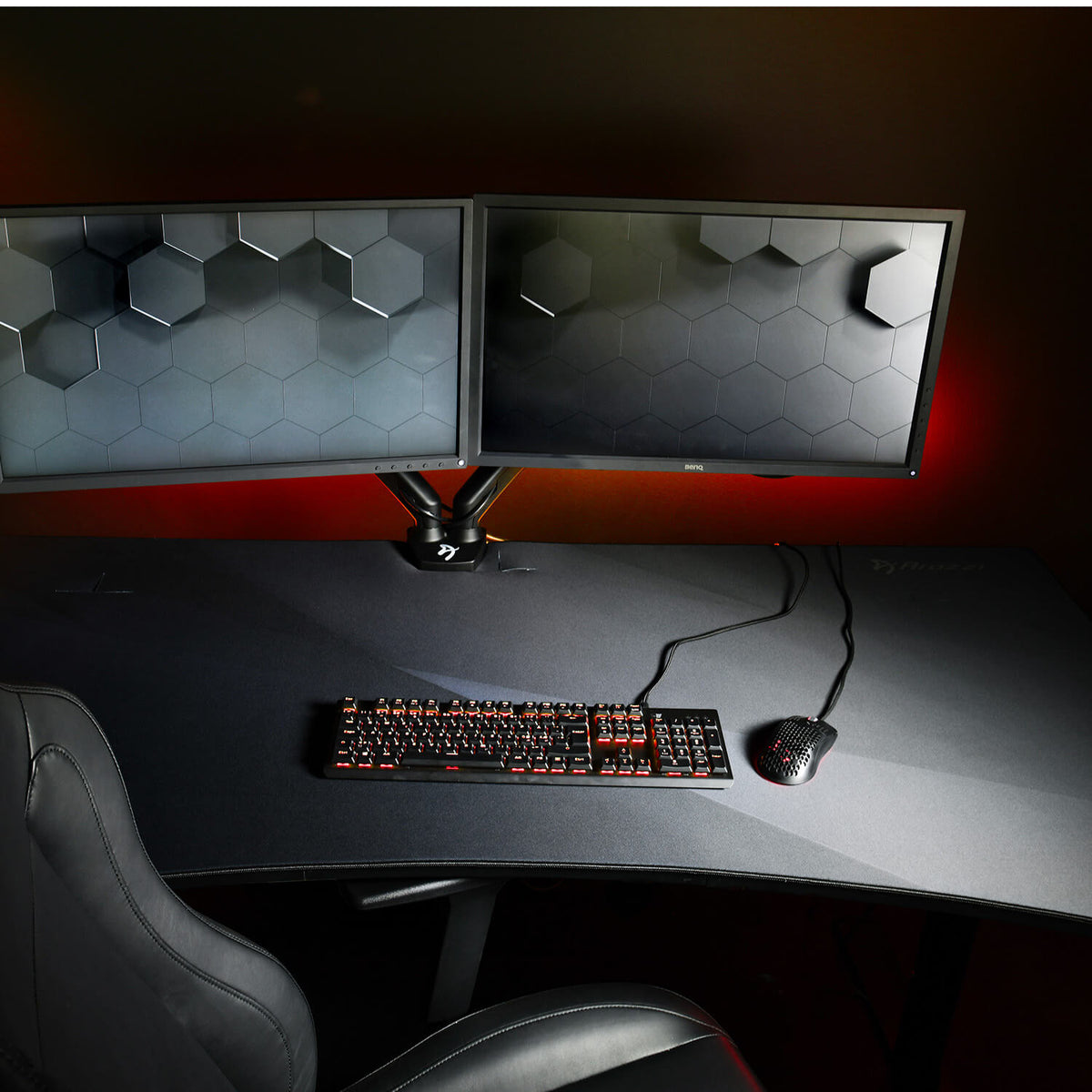 Dual monitors, keyboard, mouse on black desk with Arozzi Europe Arena Mousepad and gaming chair.