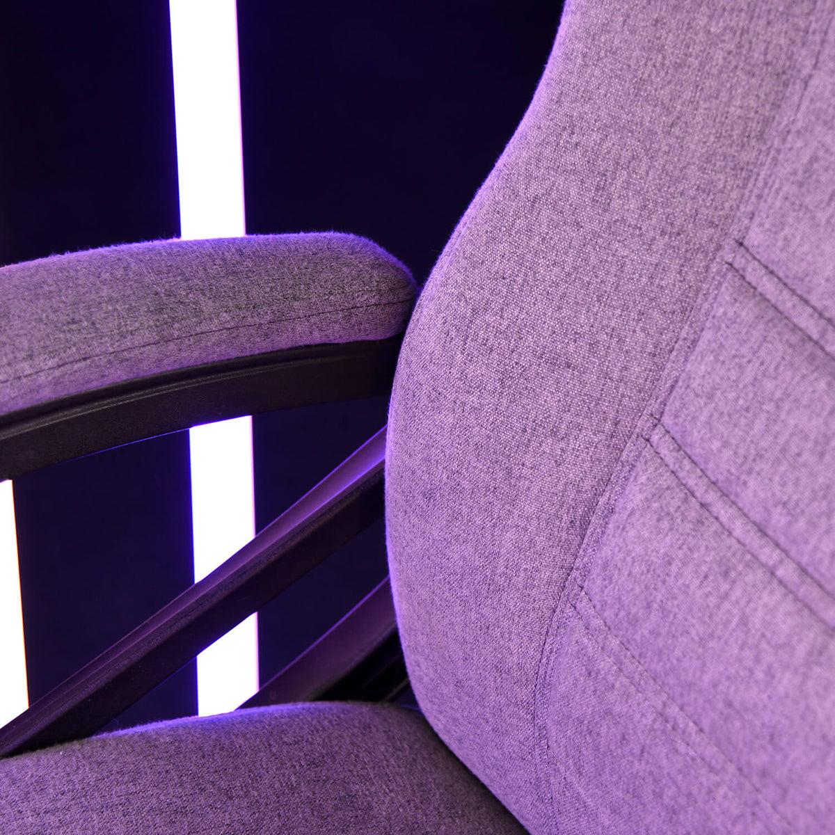 Close-up of a purple fabric chair with armrest, against a black background with vertical lights.