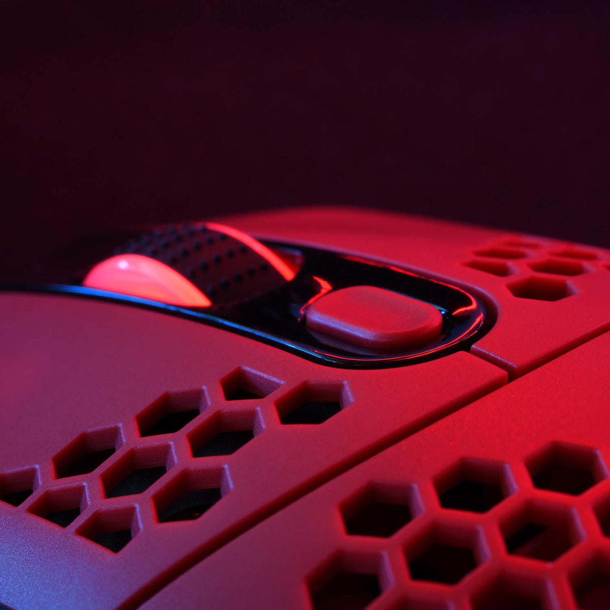 Close-up of a red gaming mouse with honeycomb design and illuminated scroll wheel.