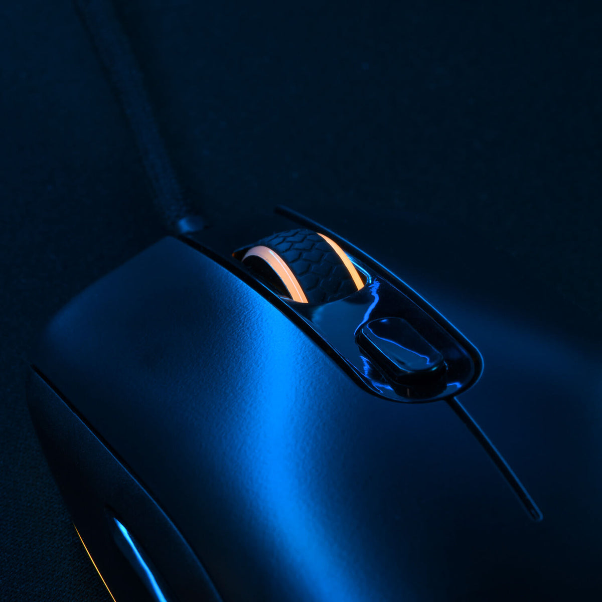 Black computer mouse with glowing orange scroll wheel, illuminated by blue light.