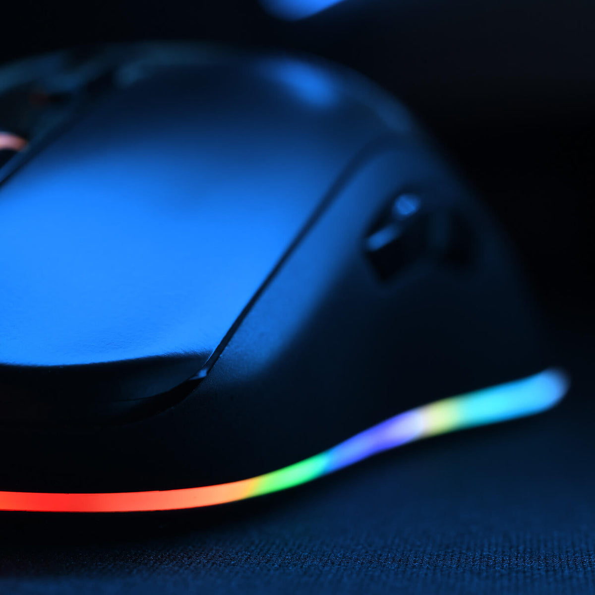 A black gaming mouse with glowing RGB lights along its base, on a dark surface.