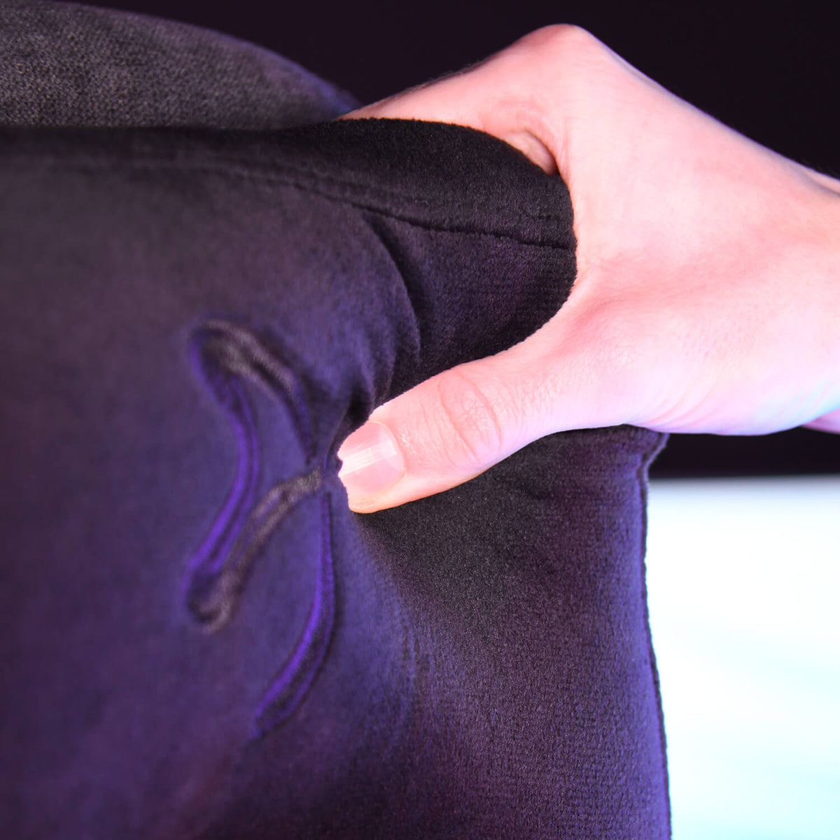 A hand squeezes a black cushion with purple stitching shaped like a butterfly.