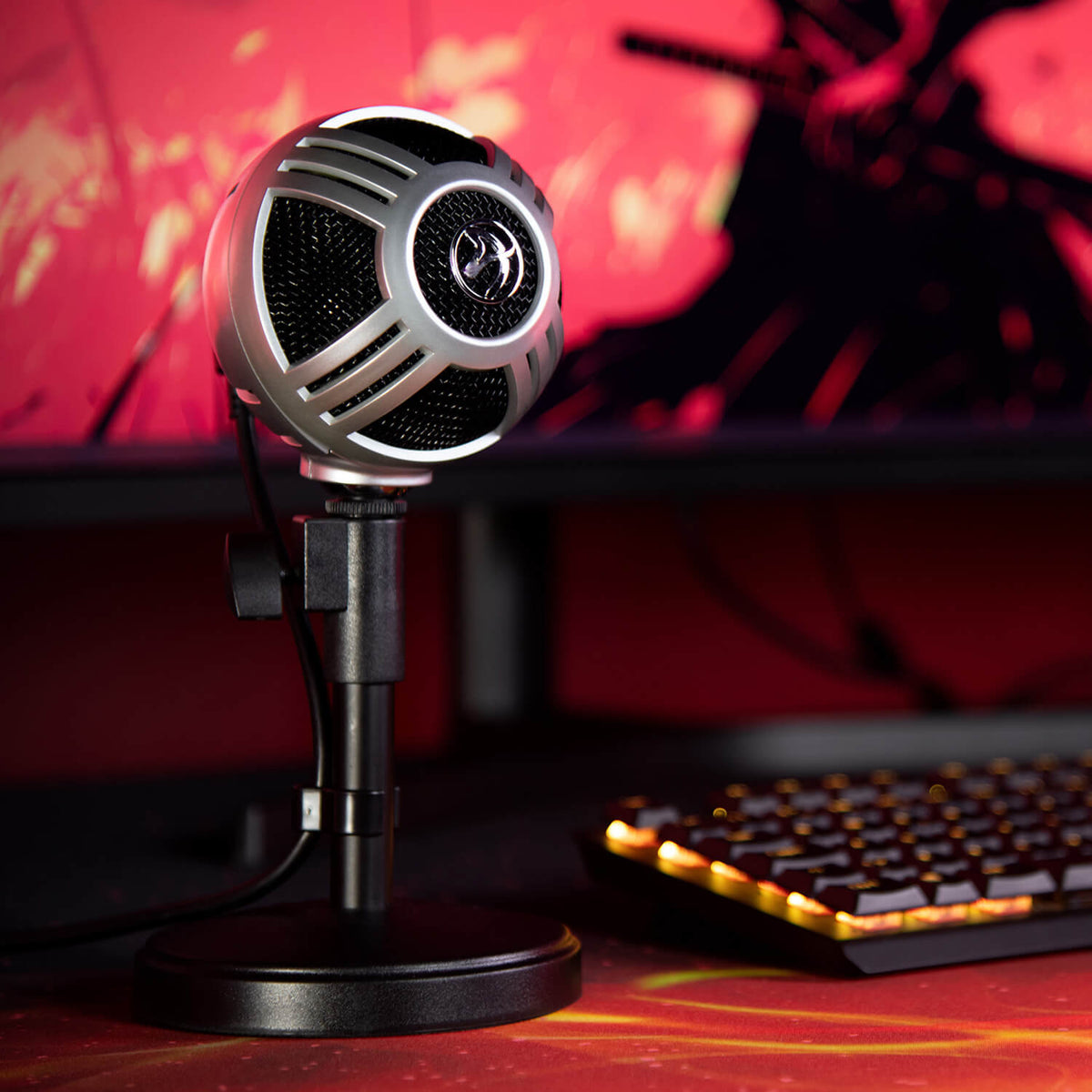 An Arozzi Sfera Pro mic stands by a glowing keyboard and monitor with a red background.