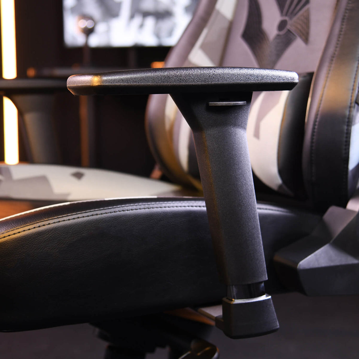 Close-up of a black adjustable armrest on a gaming chair with a patterned backrest.
