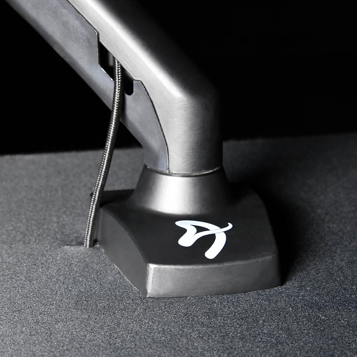 Black desk mount arm base with a white stylized A logo on a textured surface.