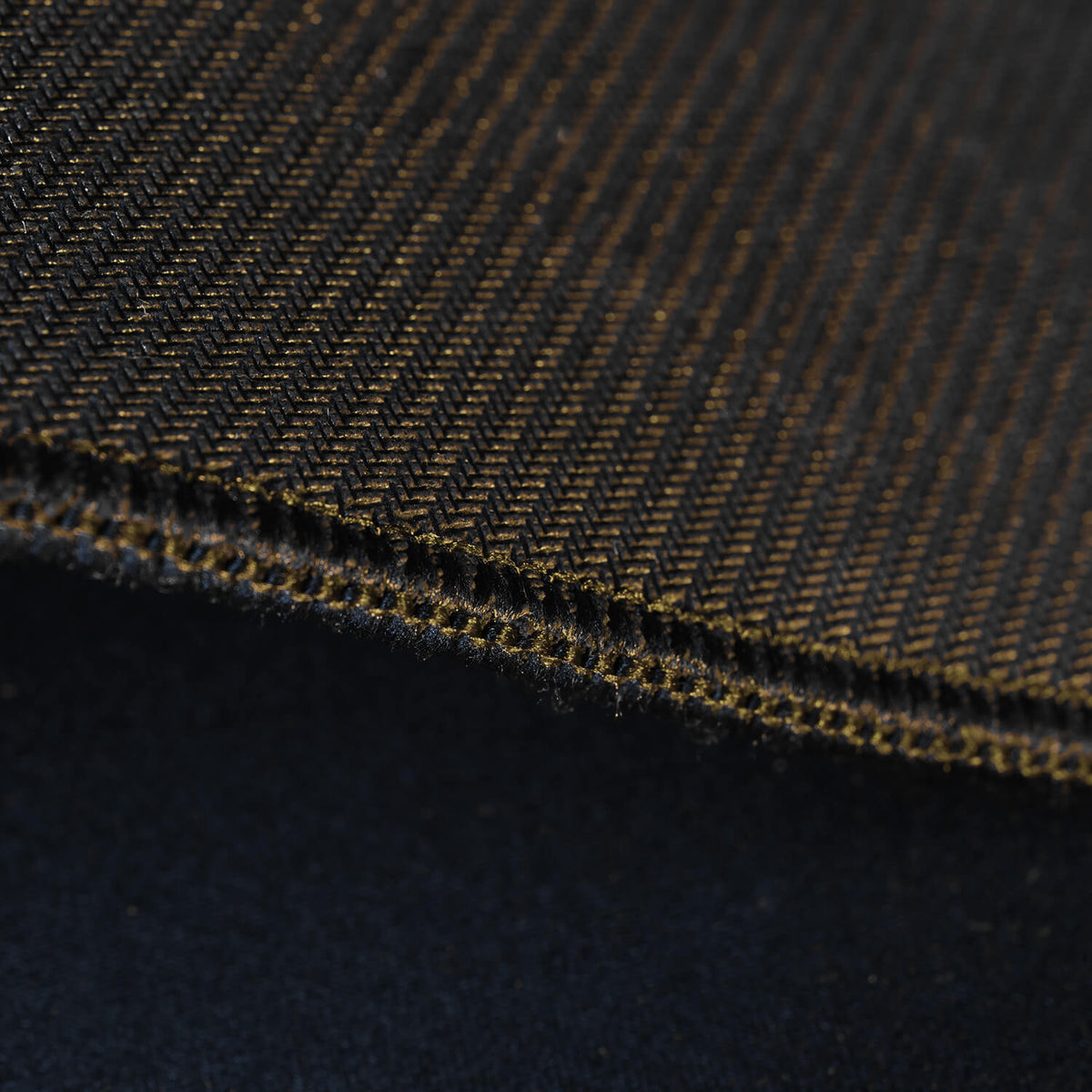 Close-up of brown herringbone fabric with visible textured weave and stitched edge.