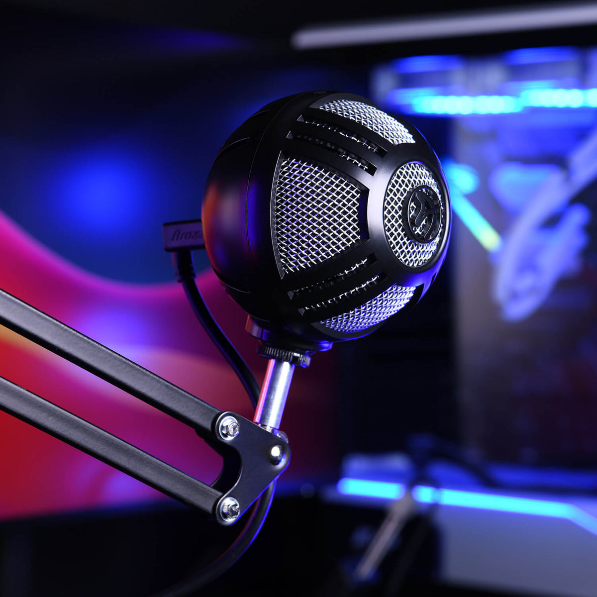 A round black microphone on an adjustable arm in a colorful, illuminated studio setup.
