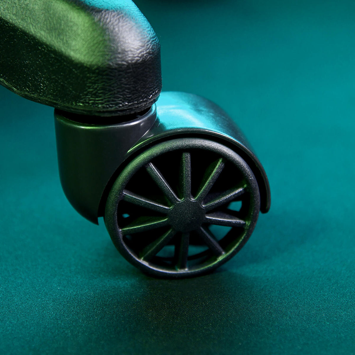 Close-up of a black office chair wheel on a teal surface.