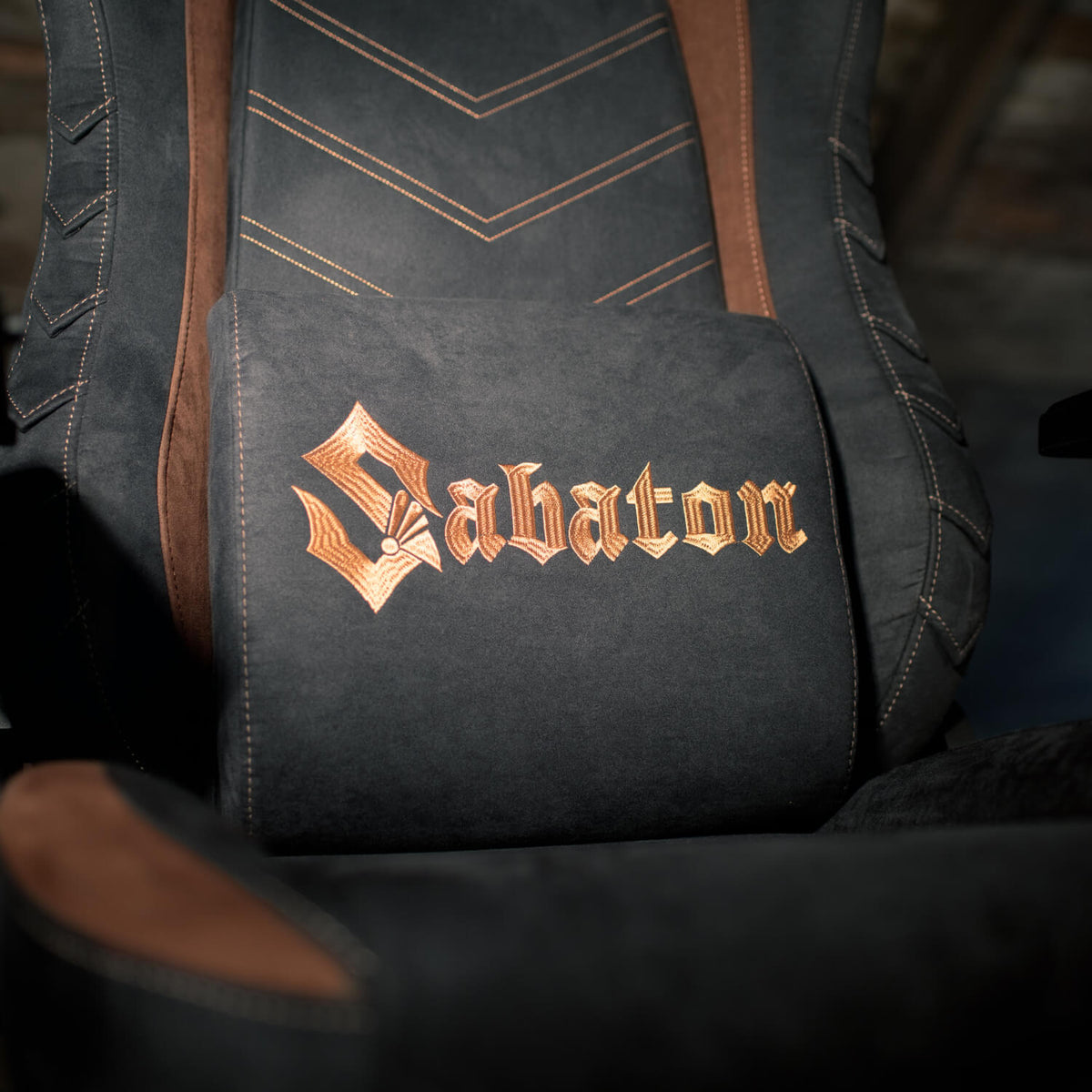 Black chair with brown accents and Sabaton embroidered in gold gothic script on lumbar pillow.