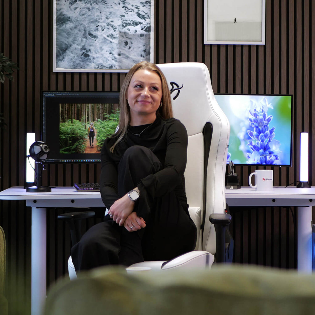 Woman in black sits on Arozzi Europe Vernazza SoftPU chair at desk with monitors and decor.