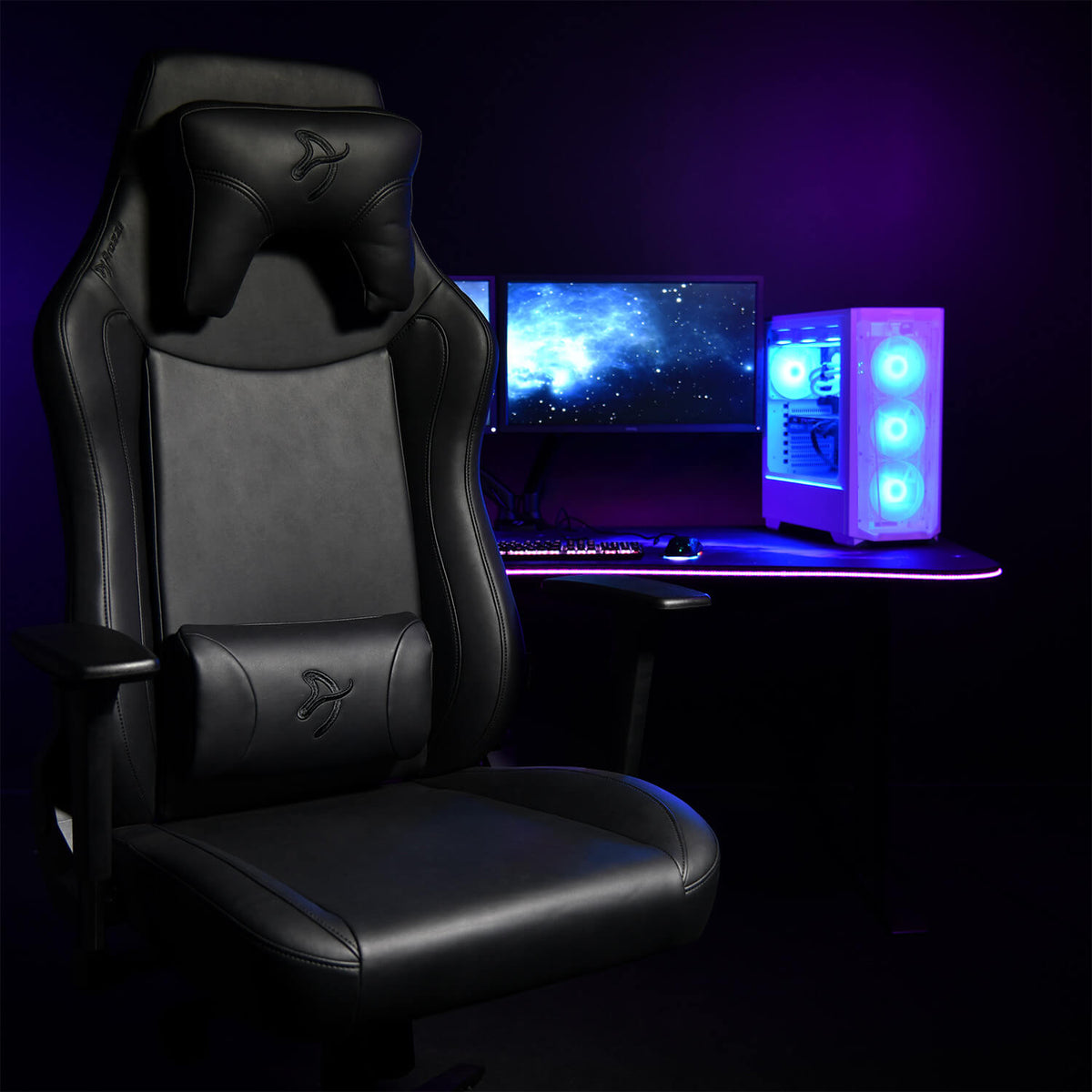 Arozzi Europe Vernazza XL SoftPU gaming chair beside a dual-monitor desk and lit-up PC.