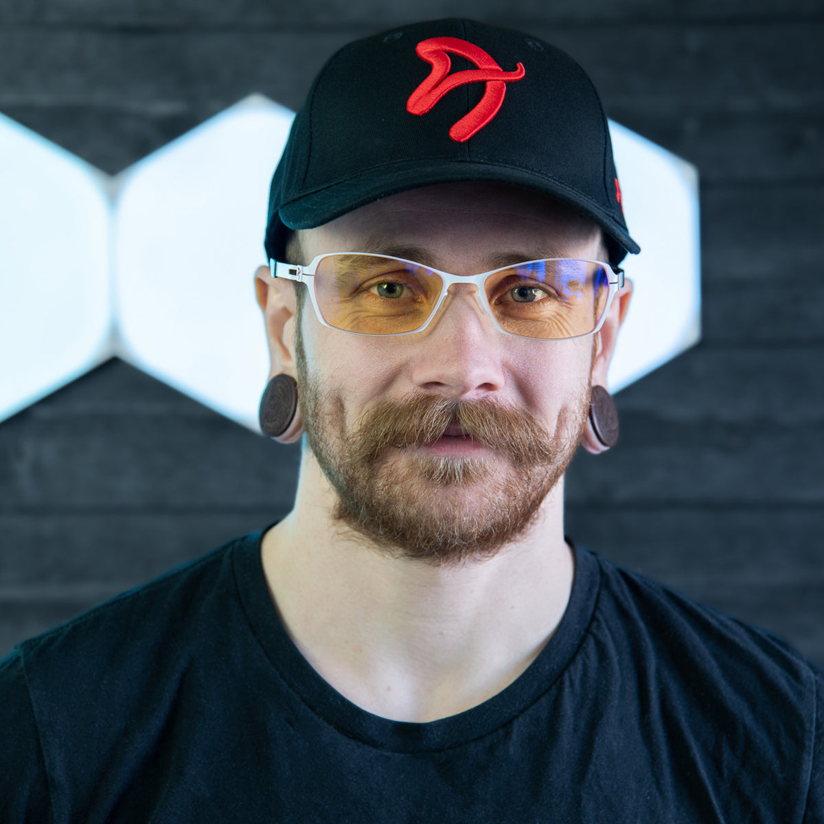 Man with mustache, cap, Visione VX-500 yellow blue light glasses by Arozzi Europe, and large gauges.