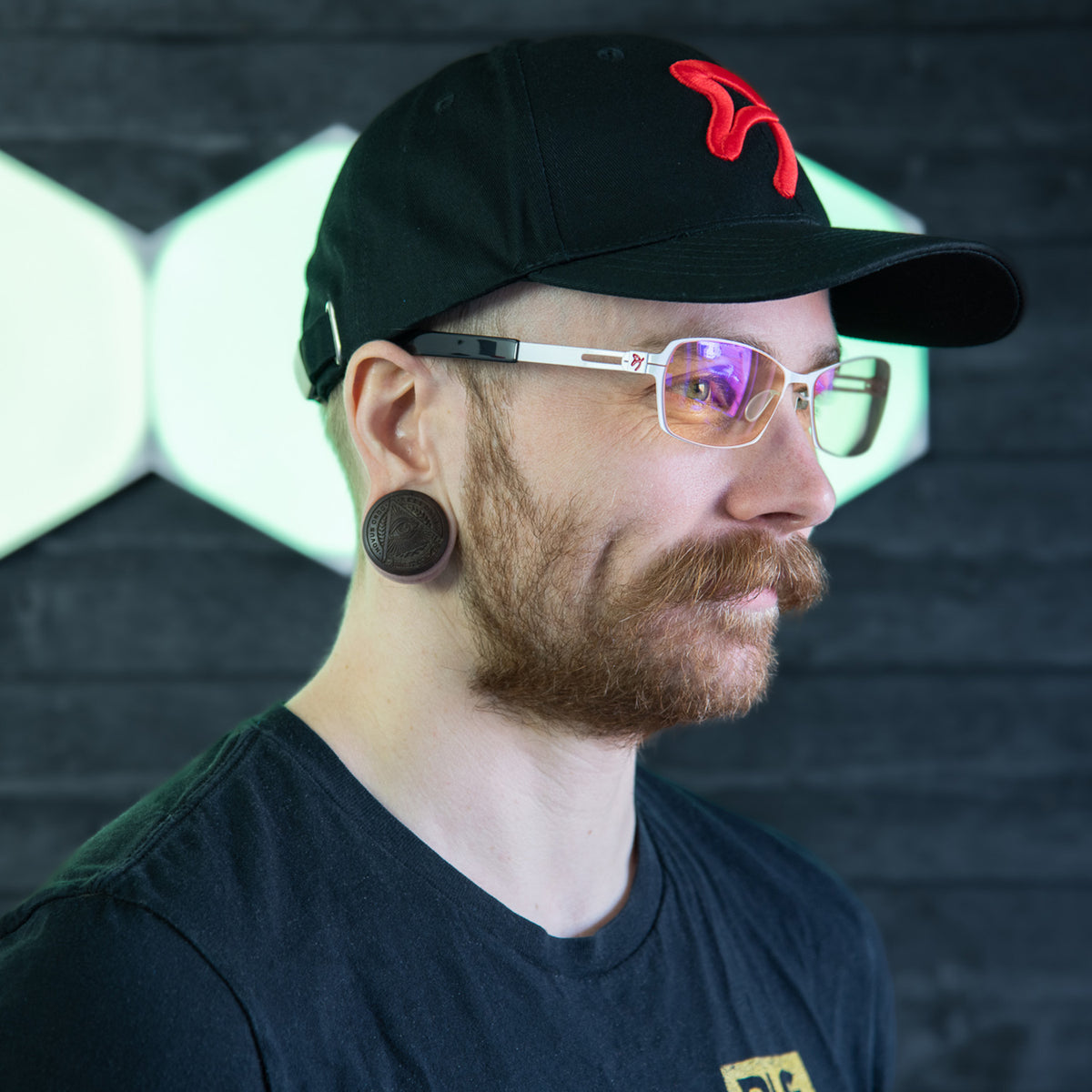 Man wearing Arozzi Europe Visione VX-500 glasses, cap, and ear gauges in bright lights.
