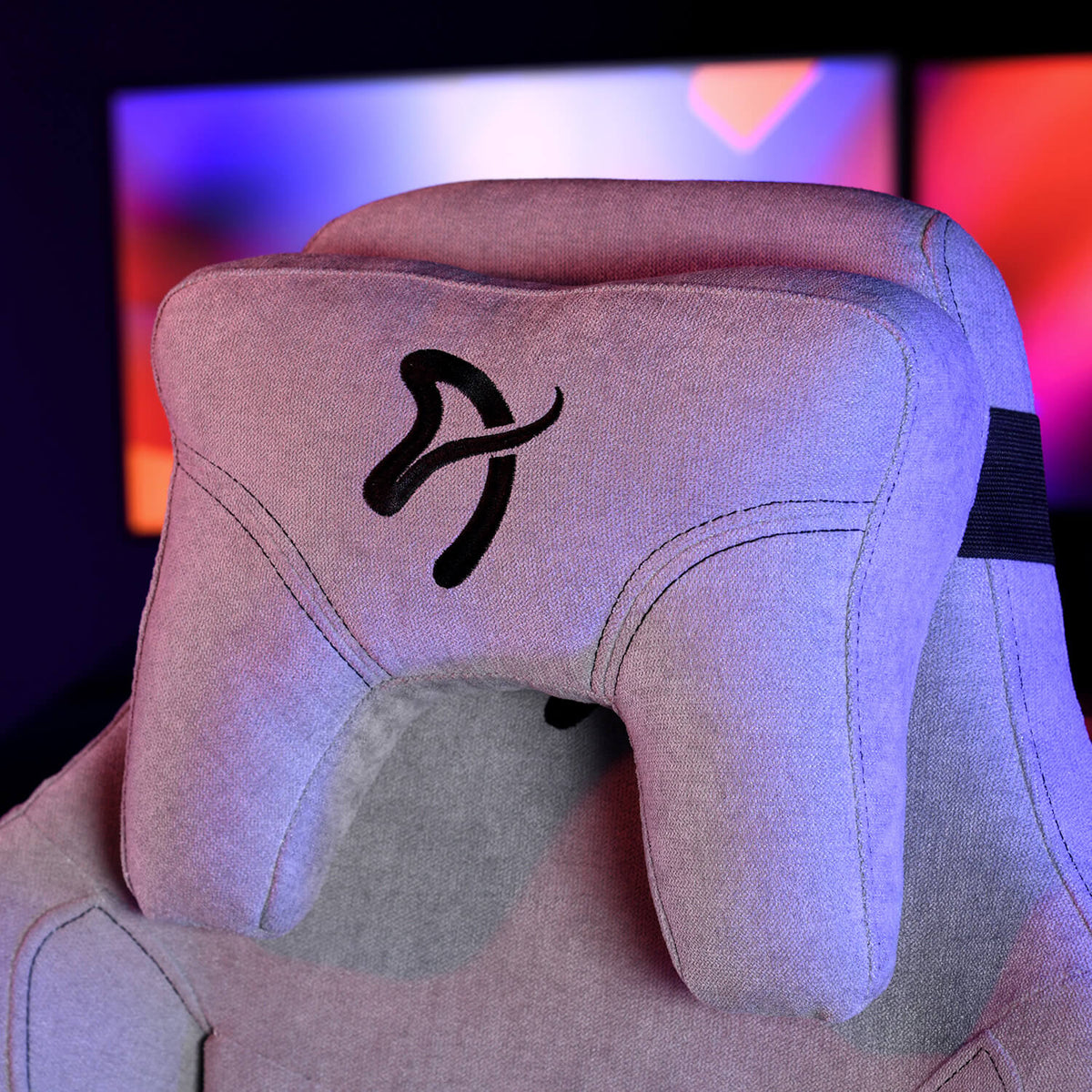 Gray gaming chair headrest with a black logo, set against blurred colorful screens in background.